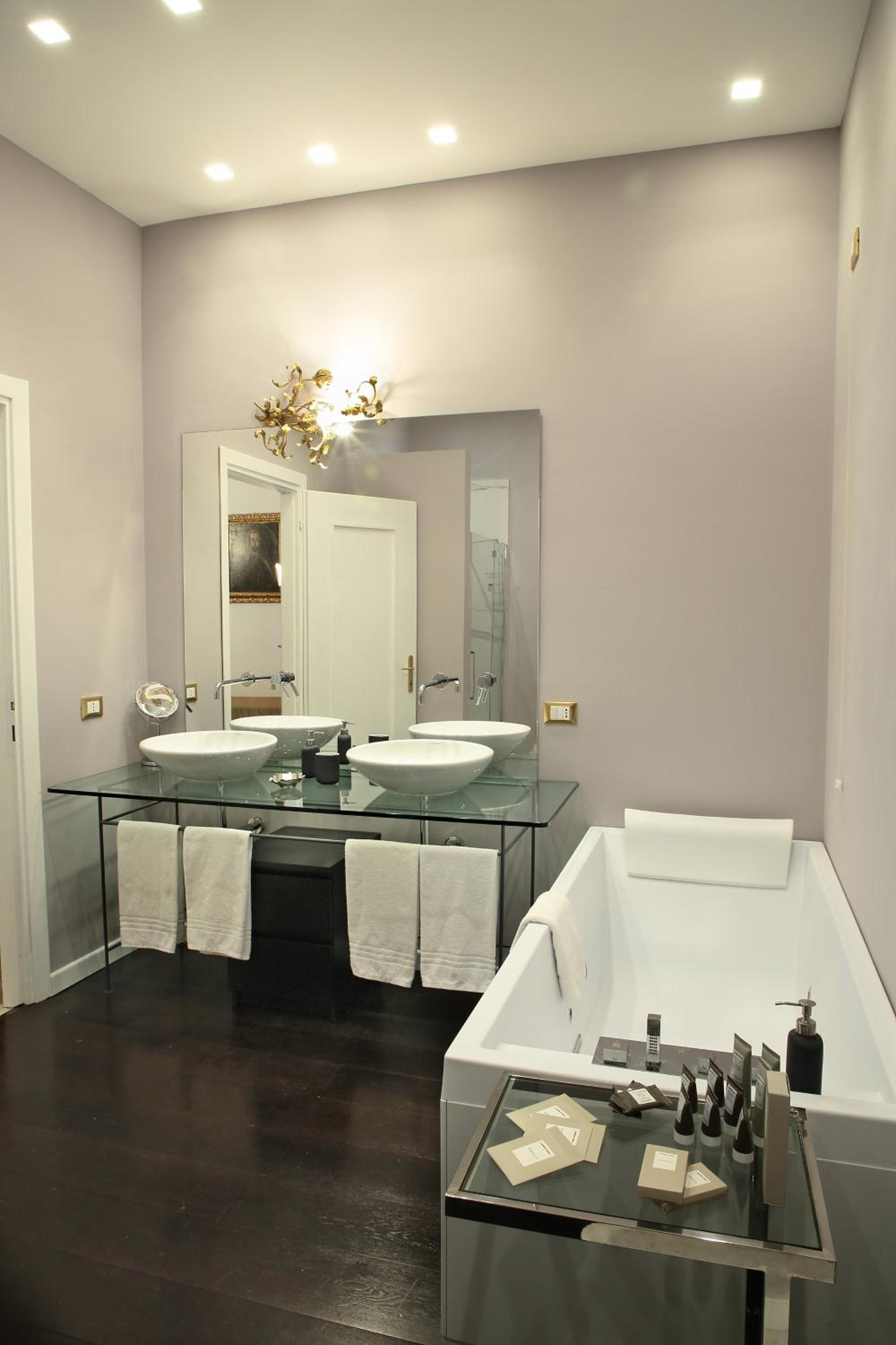 A bathroom featuring dark wood floors, a white soaking tub, and a glass-topped vanity beneath a mirror.