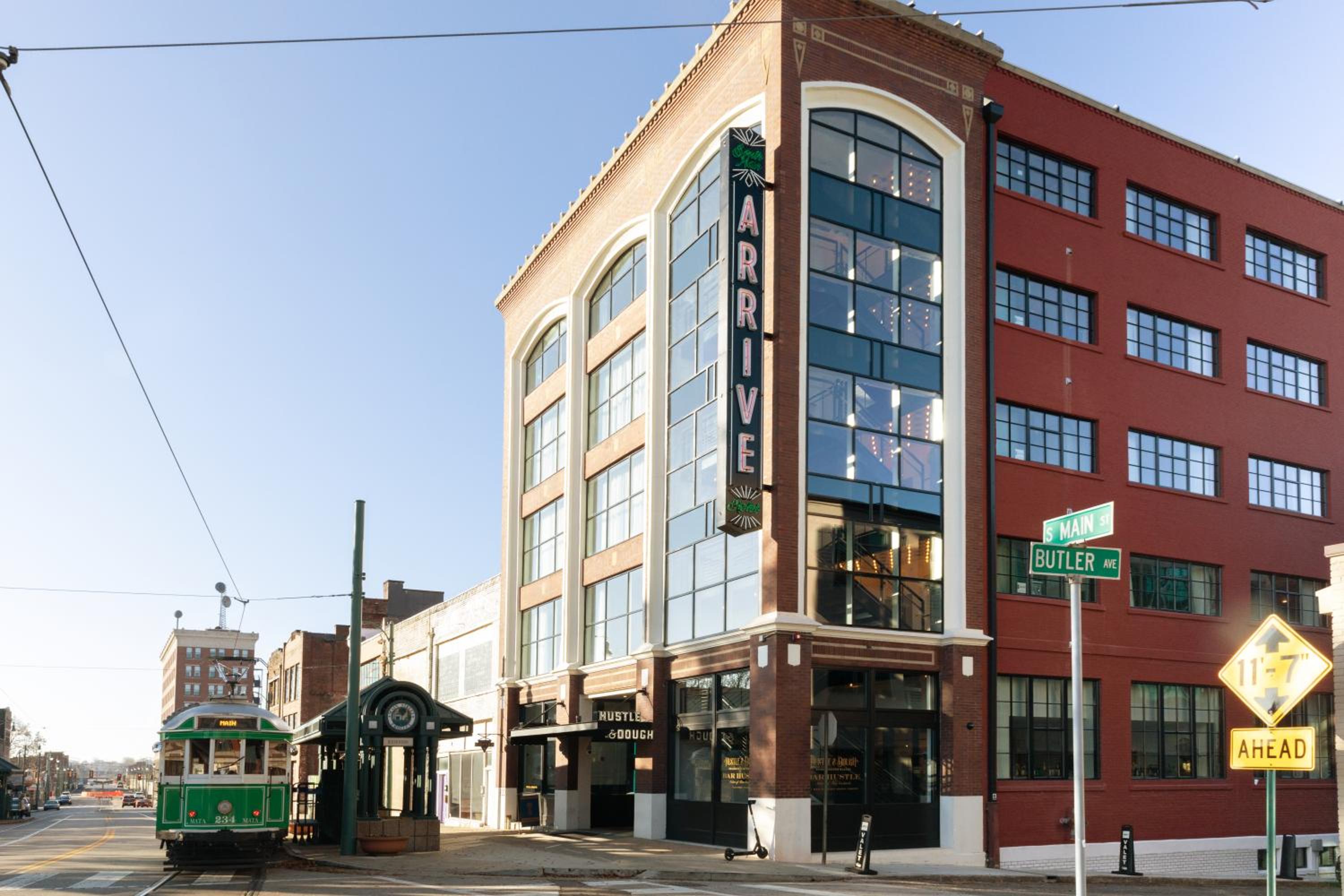 A vintage green trolley car sits outside the brick hotel building under clear daylight.