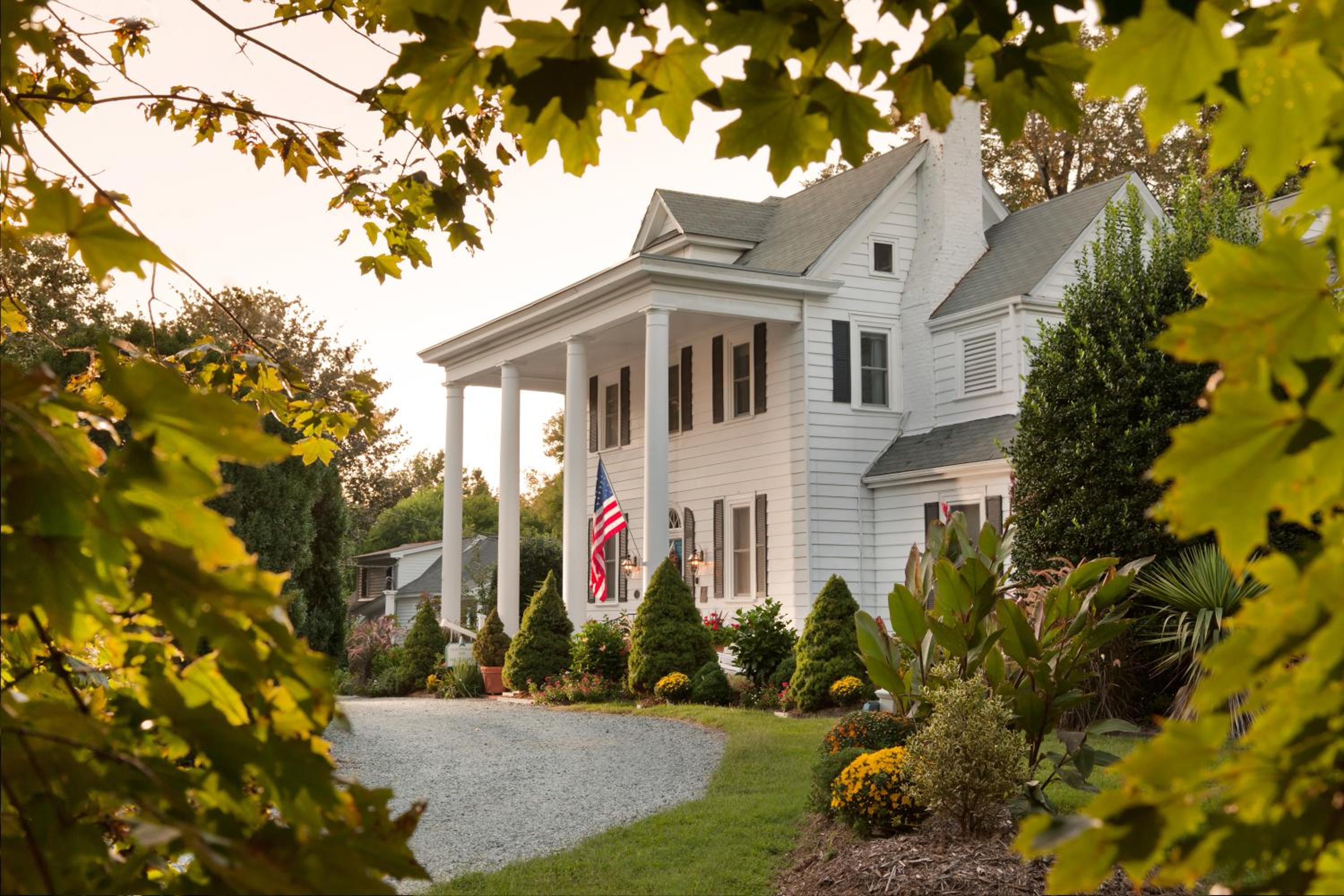 The white clapboard facade of Arrowhead Inn stands behind a curved gravel drive framed by green leaves.