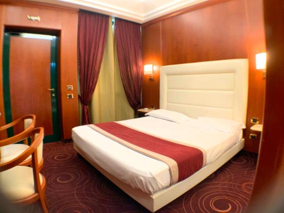 Wood-paneled walls surround a bed with a tall white headboard, patterned carpet, and deep red curtains.