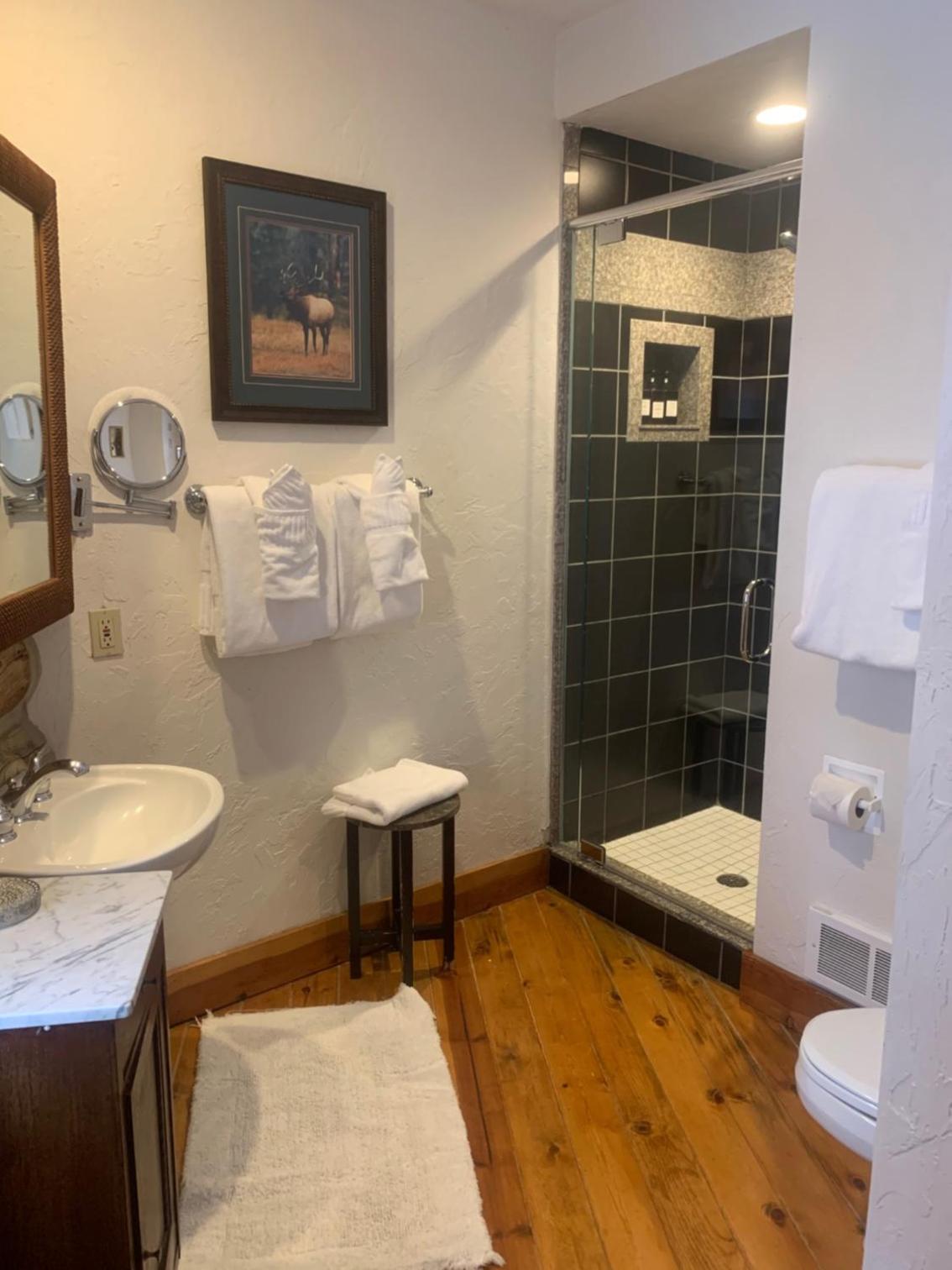 Bathroom with hardwood flooring, a marble-top vanity, and a glass-enclosed shower lined with dark tile.