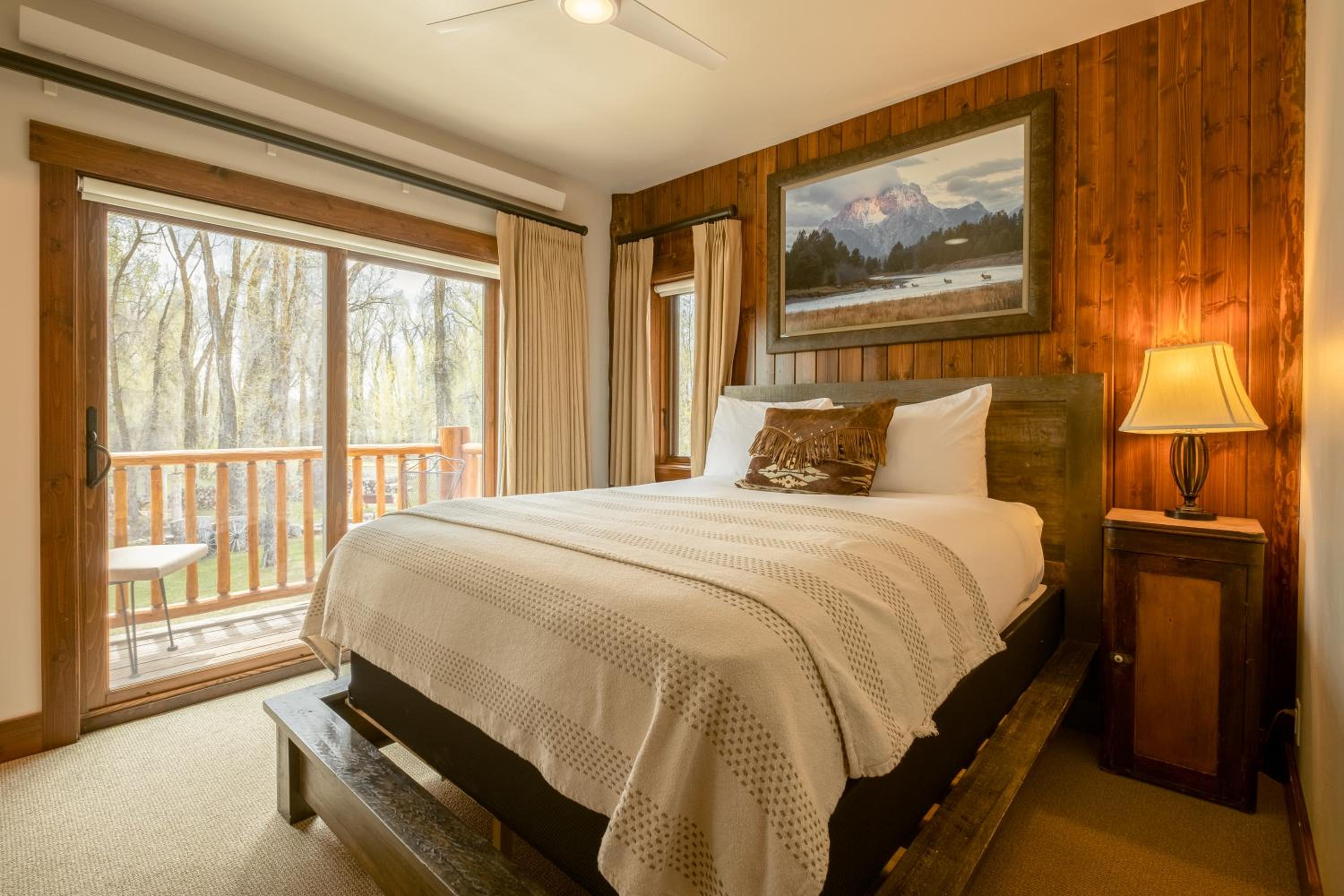 Bedroom featuring wood-paneled walls, a mountain landscape painting, and a sliding glass door opening onto a deck.