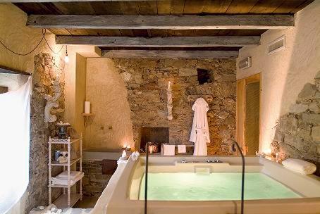 An indoor spa bath sits beneath exposed ceiling beams and rustic stone walls.
