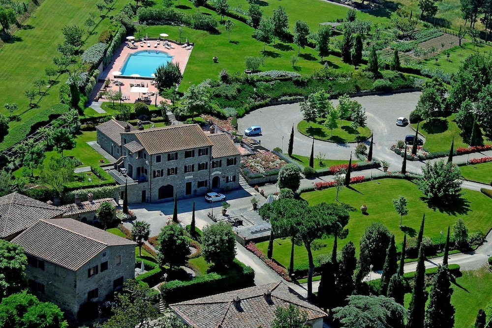 Aerial view of Borgo Il Melone showing stone country buildings, a swimming pool, manicured lawns, and trees.