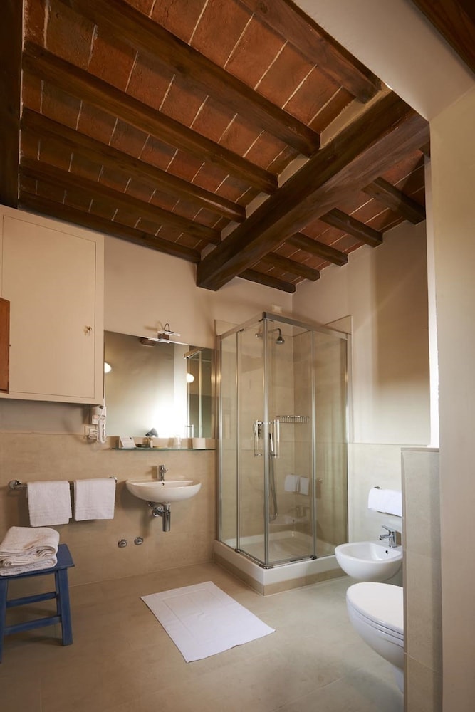A bathroom with timber beams, a corner glass shower enclosure, white fixtures, and tiled flooring.