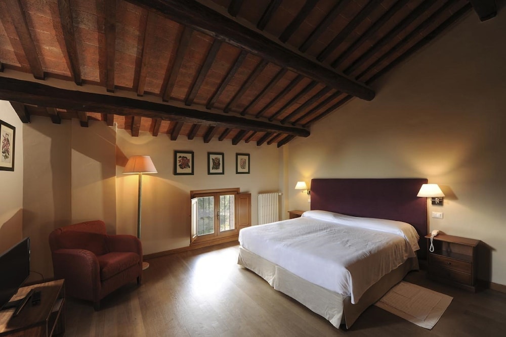 A bedroom with a beamed terracotta ceiling, wood floors, an armchair, and a bed with a purple headboard.
