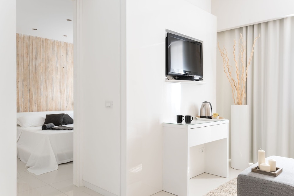 Modern white living area with a wall-mounted television and doorway into a wood-paneled bedroom.