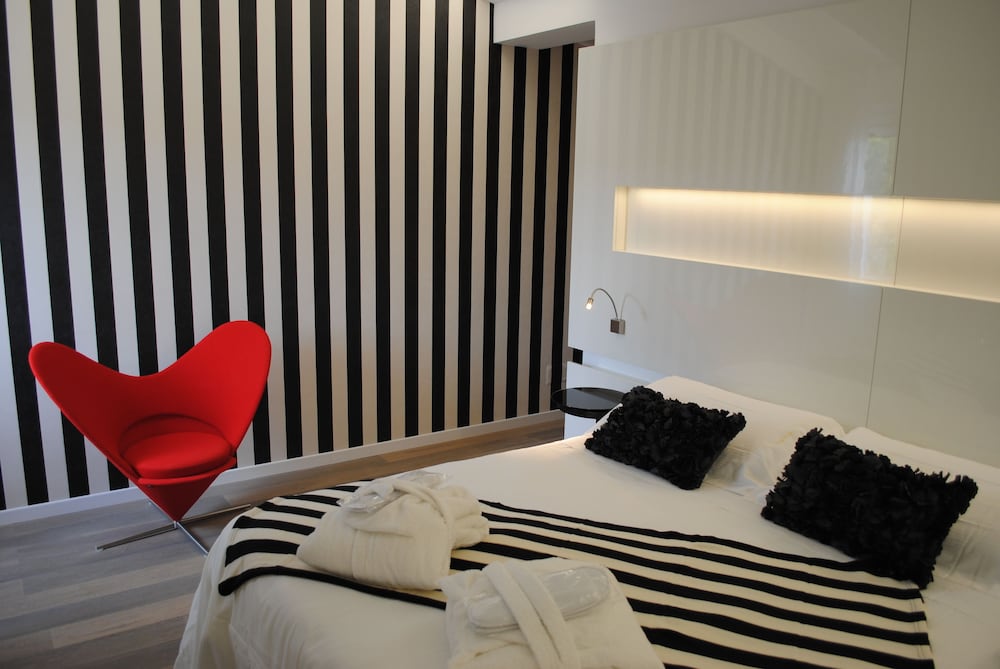 Bedroom with vertical black-and-white striped wallpaper, a red accent chair, and a bed.