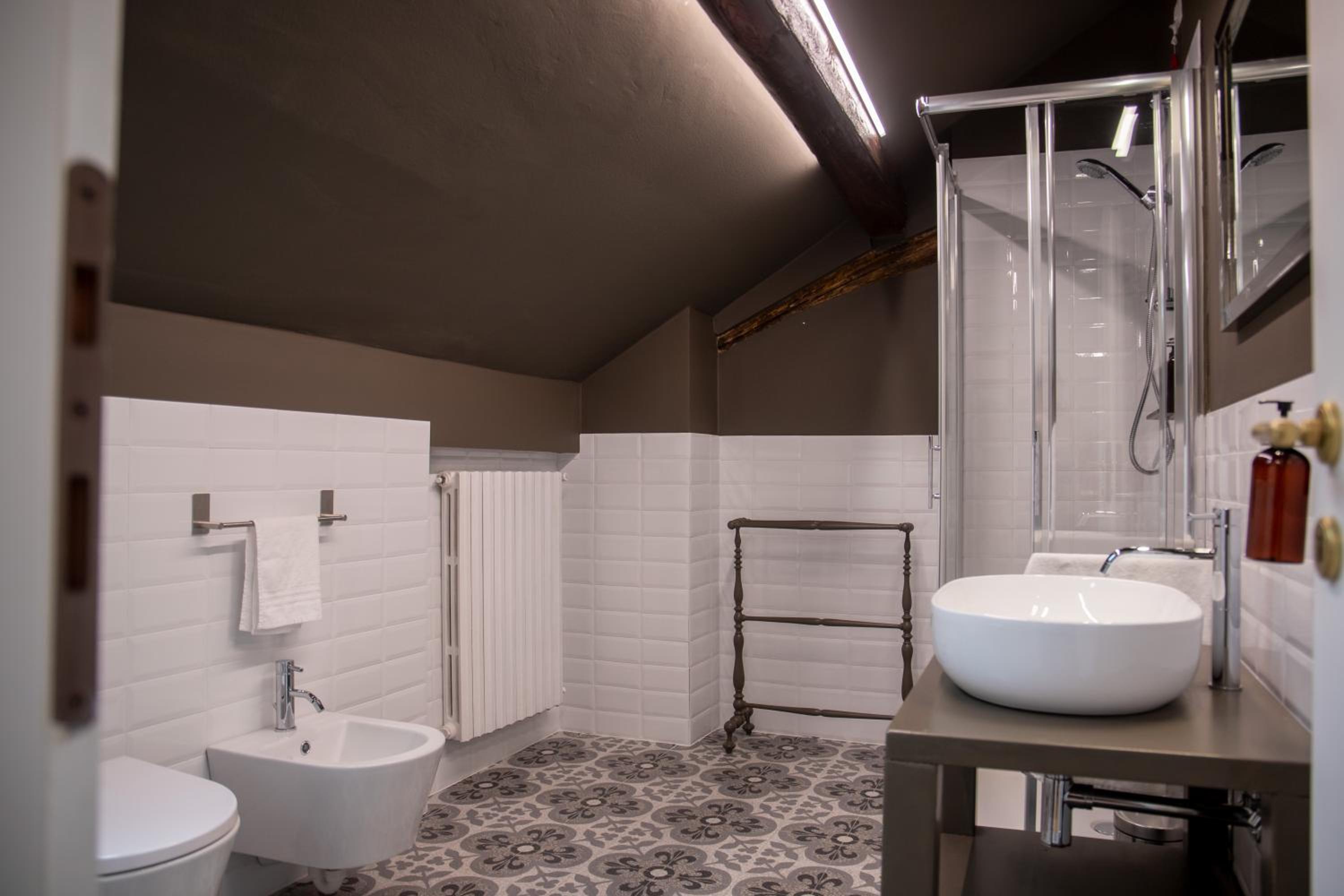 An attic bathroom with patterned floor tiles, white subway walls, an exposed ceiling beam, and a vessel sink.