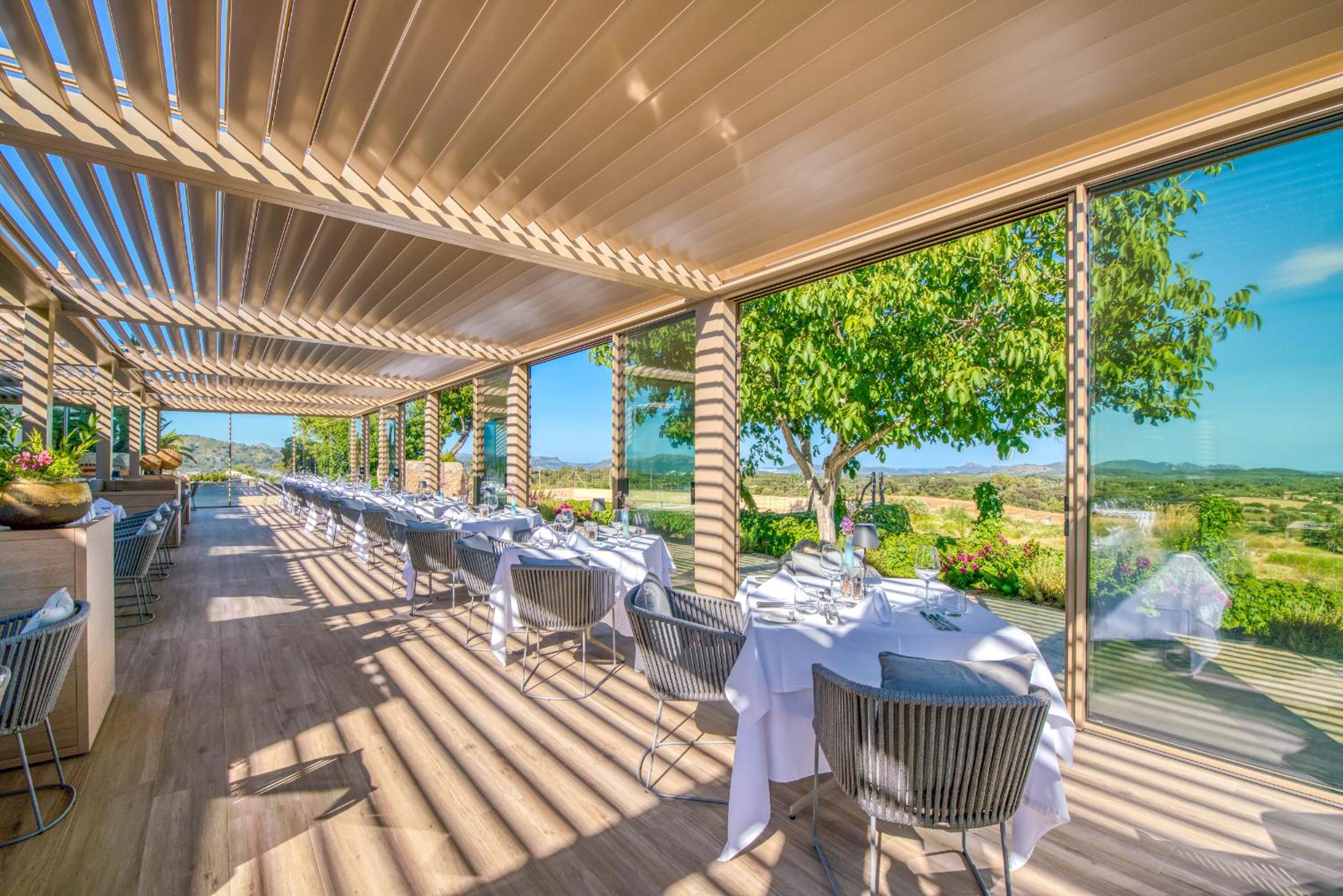 A covered terrace with slatted pergola, set dining tables, and open views over the countryside.