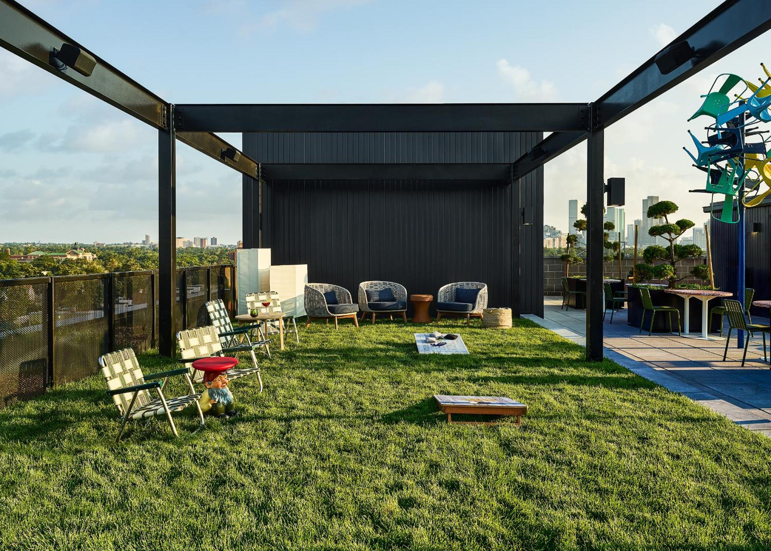 A rooftop terrace with a green lawn under a dark steel pergola, furnished with patio seating and lawn games.