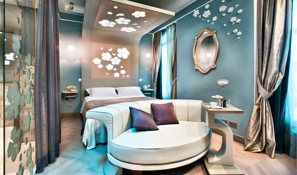 Blue bedroom at Château Monfort featuring a curved sofa, lighted floral headboard canopy, and parquet flooring.