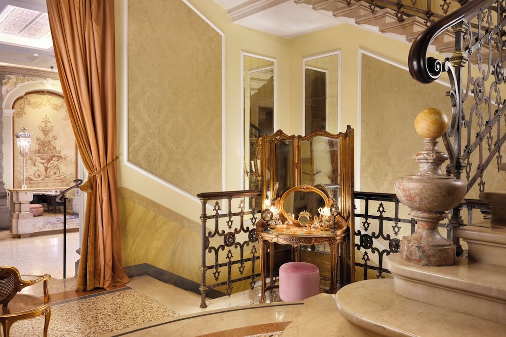 Staircase landing with an ornate vanity table, marble balustrade, and draped gold curtains.
