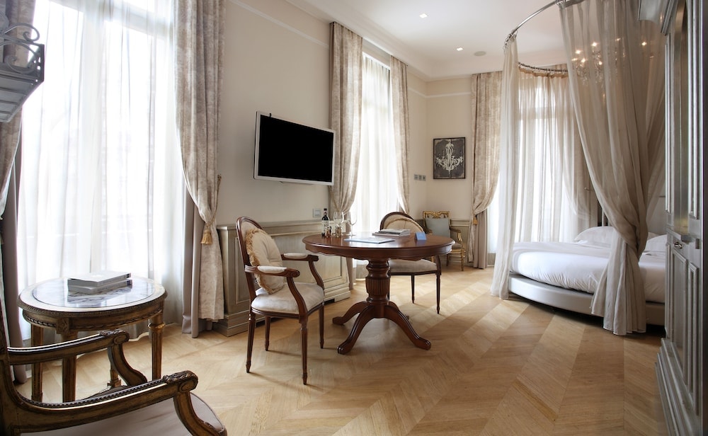 Guest room with a round bed draped in sheer curtains, parquet floor, and a wooden table beside tall windows.