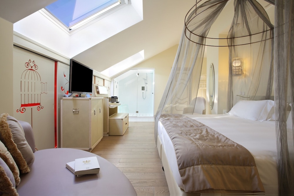 An attic bedroom with a skylight, a draped canopy bed, wooden floors, and an en-suite glass shower.