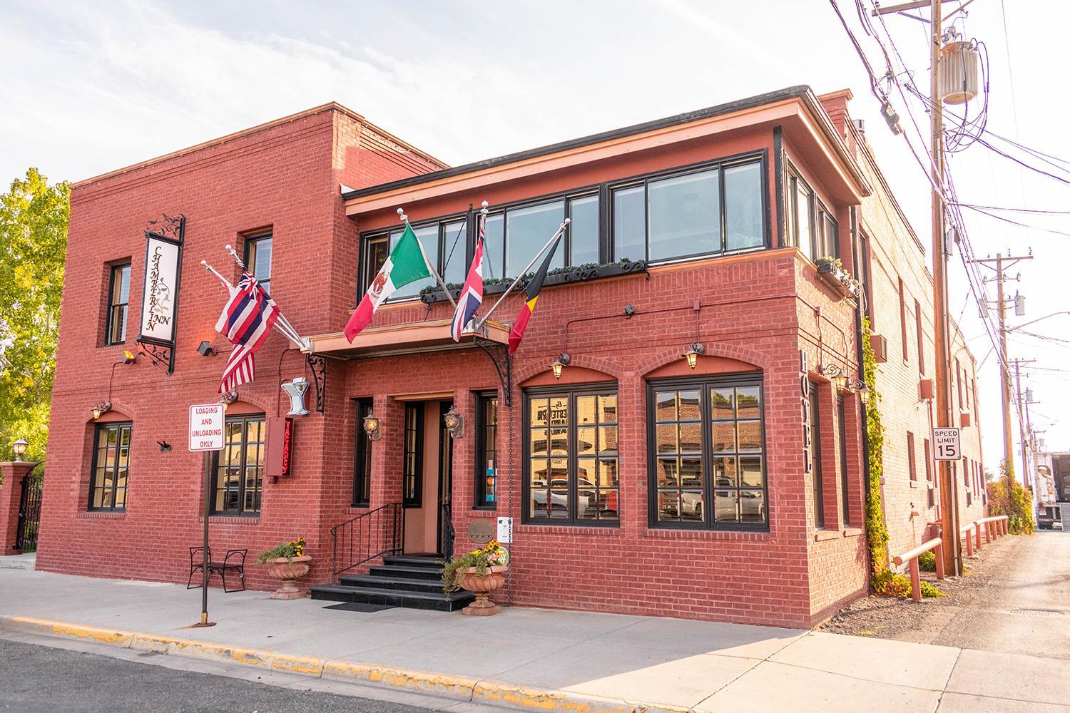 The red brick facade of Chamberlin Inn features international flags above the entrance and large street windows.