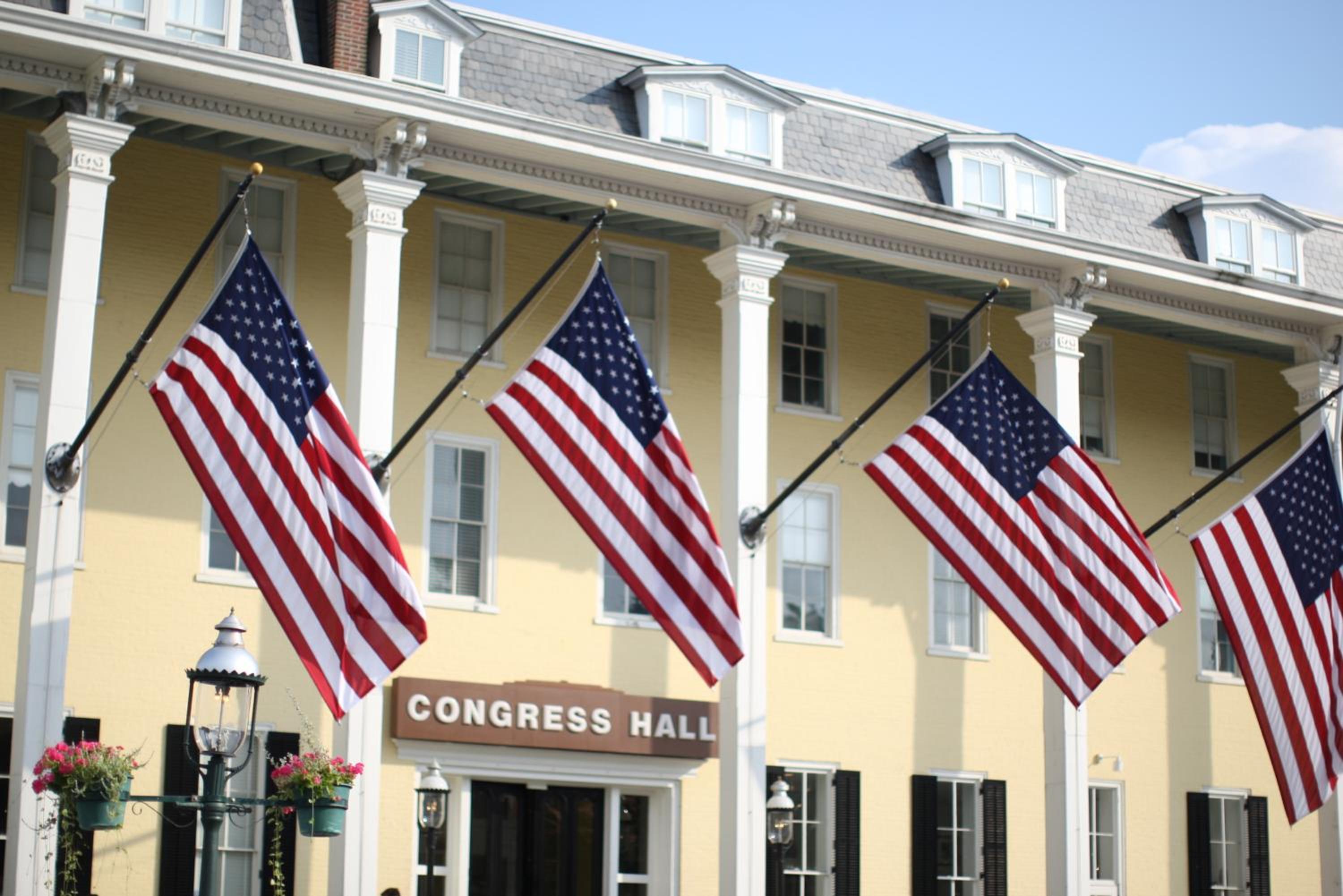 American flags hang from white columns along the yellow facade of Congress Hall.