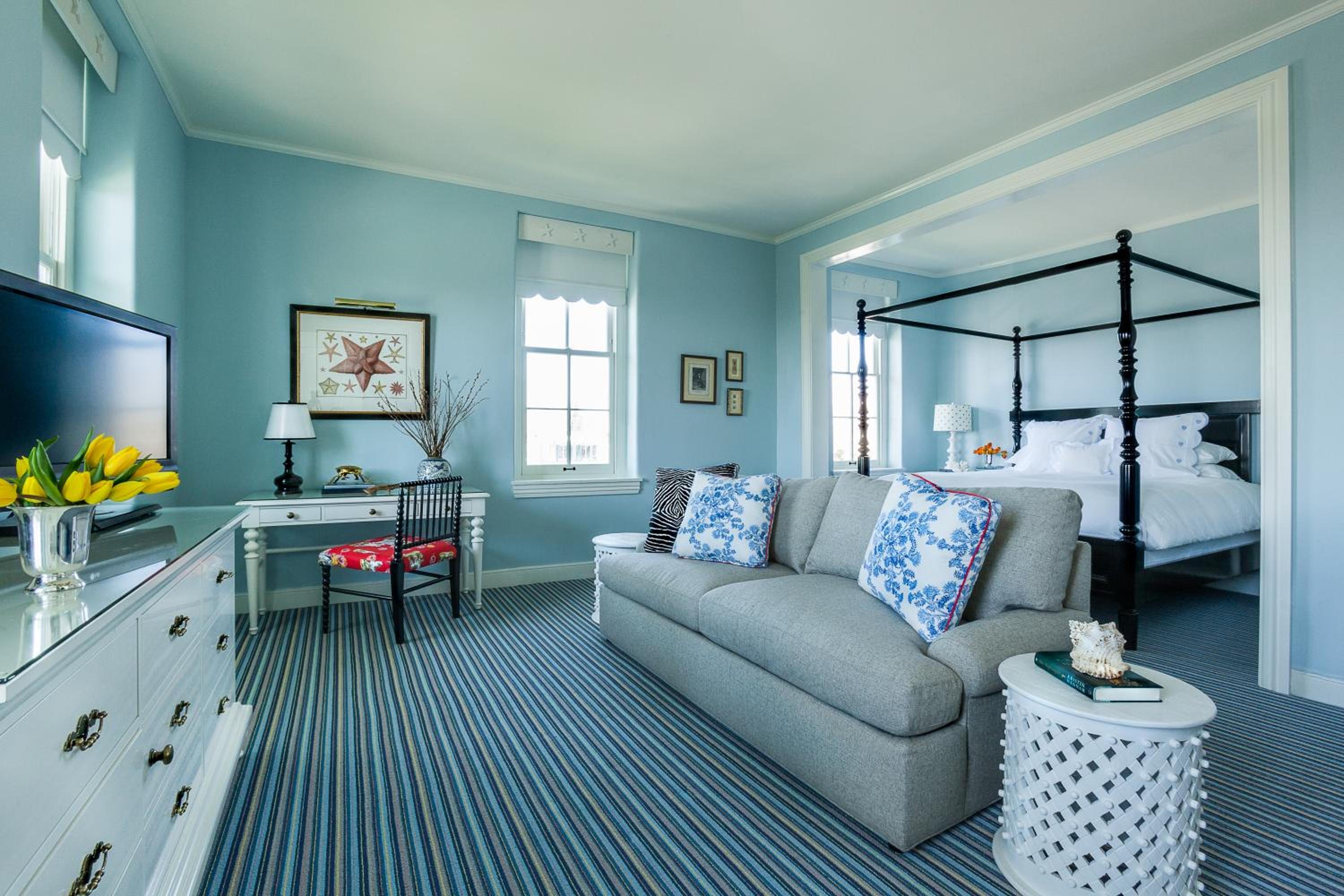 A suite with blue walls, striped carpet, a grey sofa, and a tall canopy bed set into an alcove.
