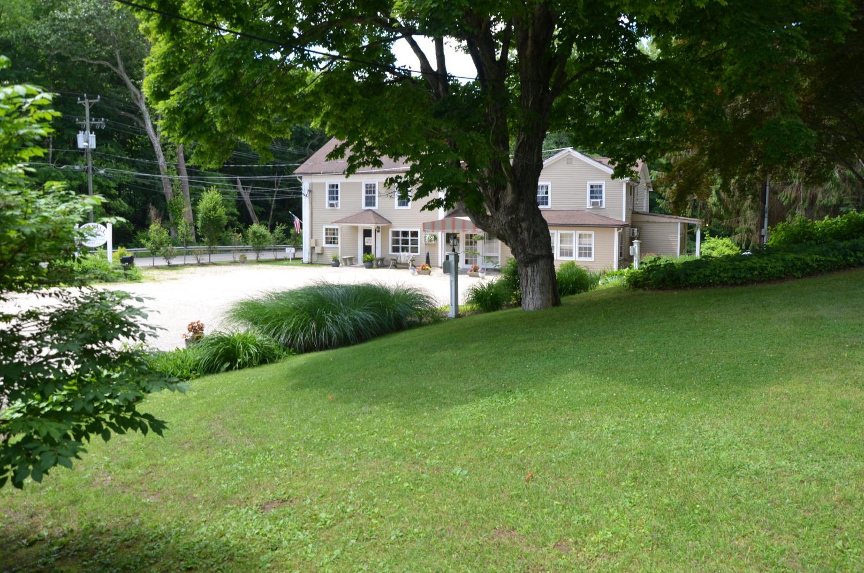 A sloping green lawn in the foreground leads down to a clapboard inn surrounded by mature trees.