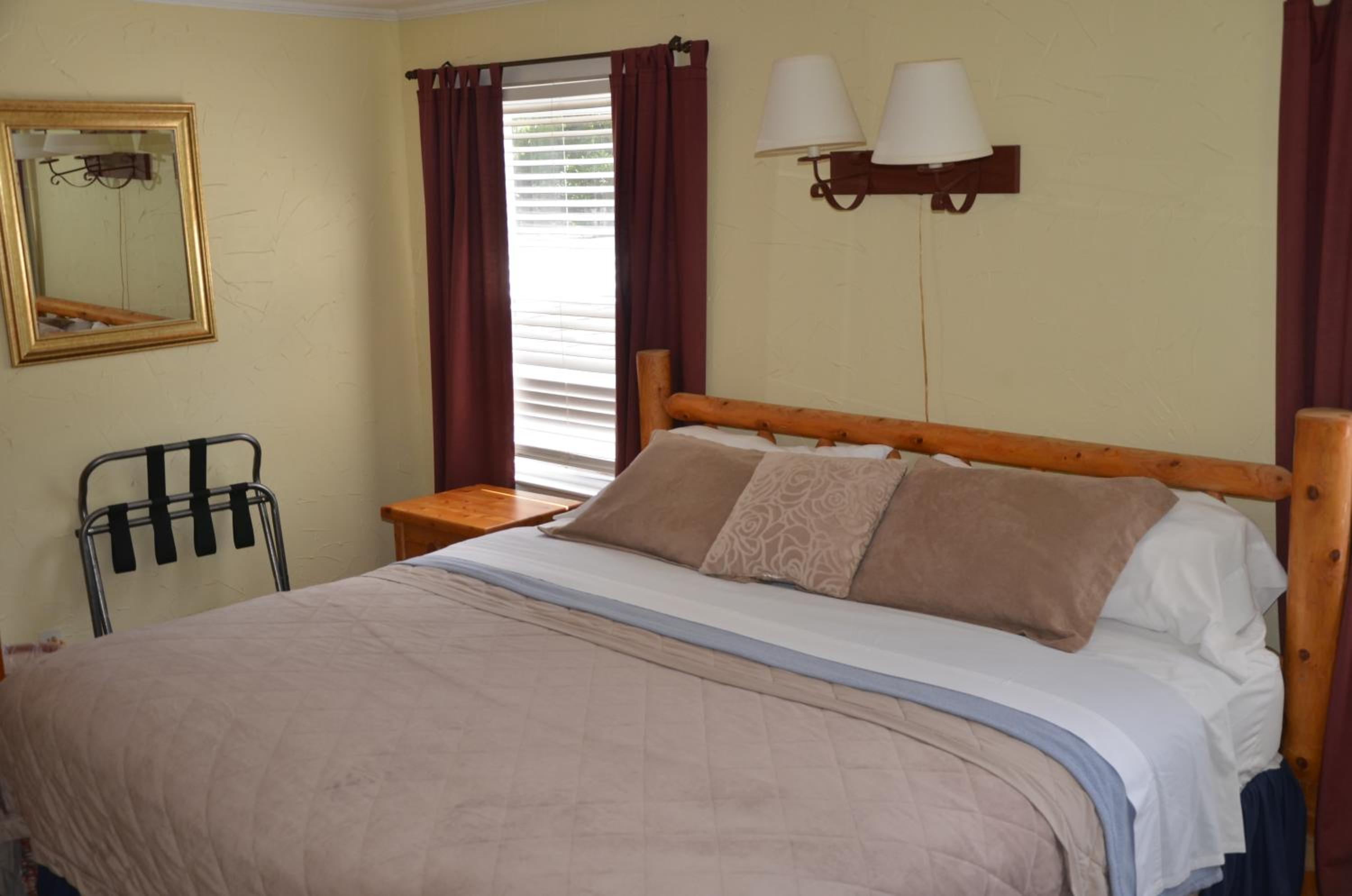A rustic wooden log bed with taupe bedding sits against textured pale yellow walls next to maroon curtains.