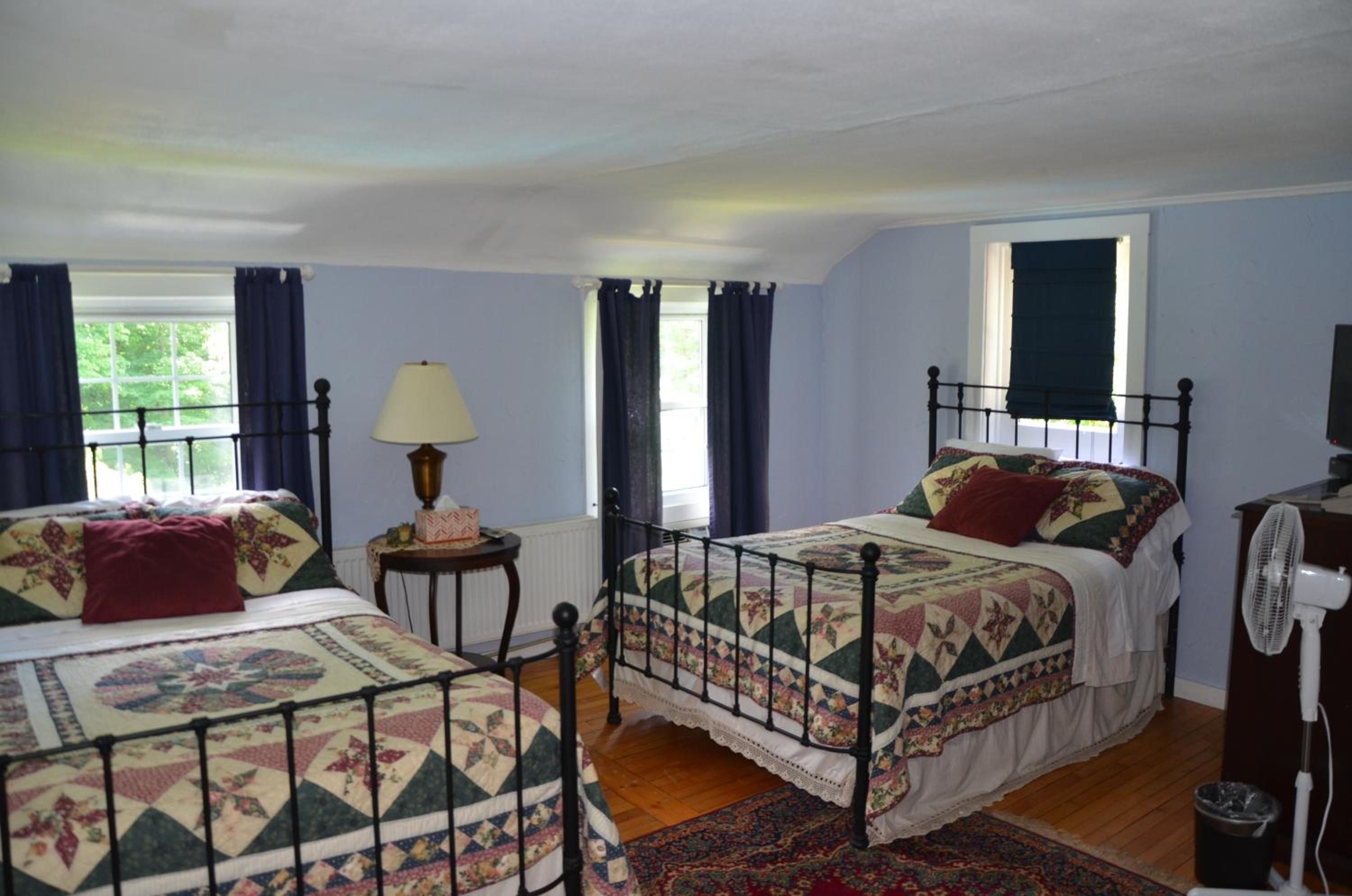 Wrought-iron beds with patchwork quilts stand on wood floors in a bedroom with pale blue walls.