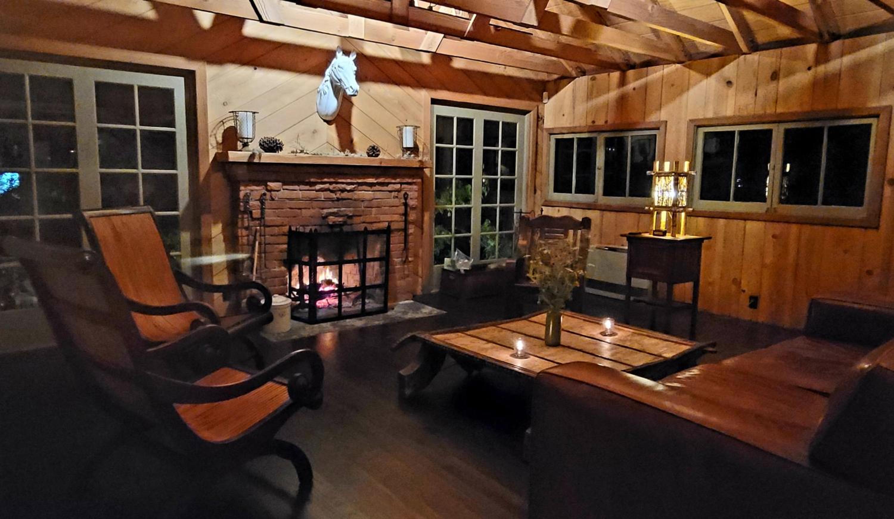 A wood-paneled room features a burning brick fireplace, exposed rafters, and leather armchairs.