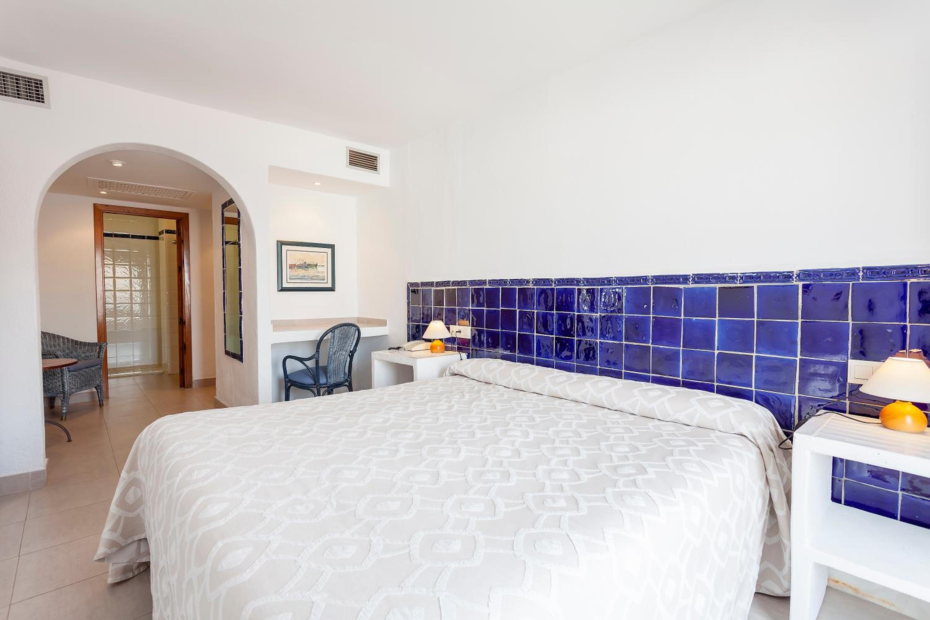 A bedroom at Doña Pakyta features white bedding against deep blue ceramic wall tiles and an arched doorway.