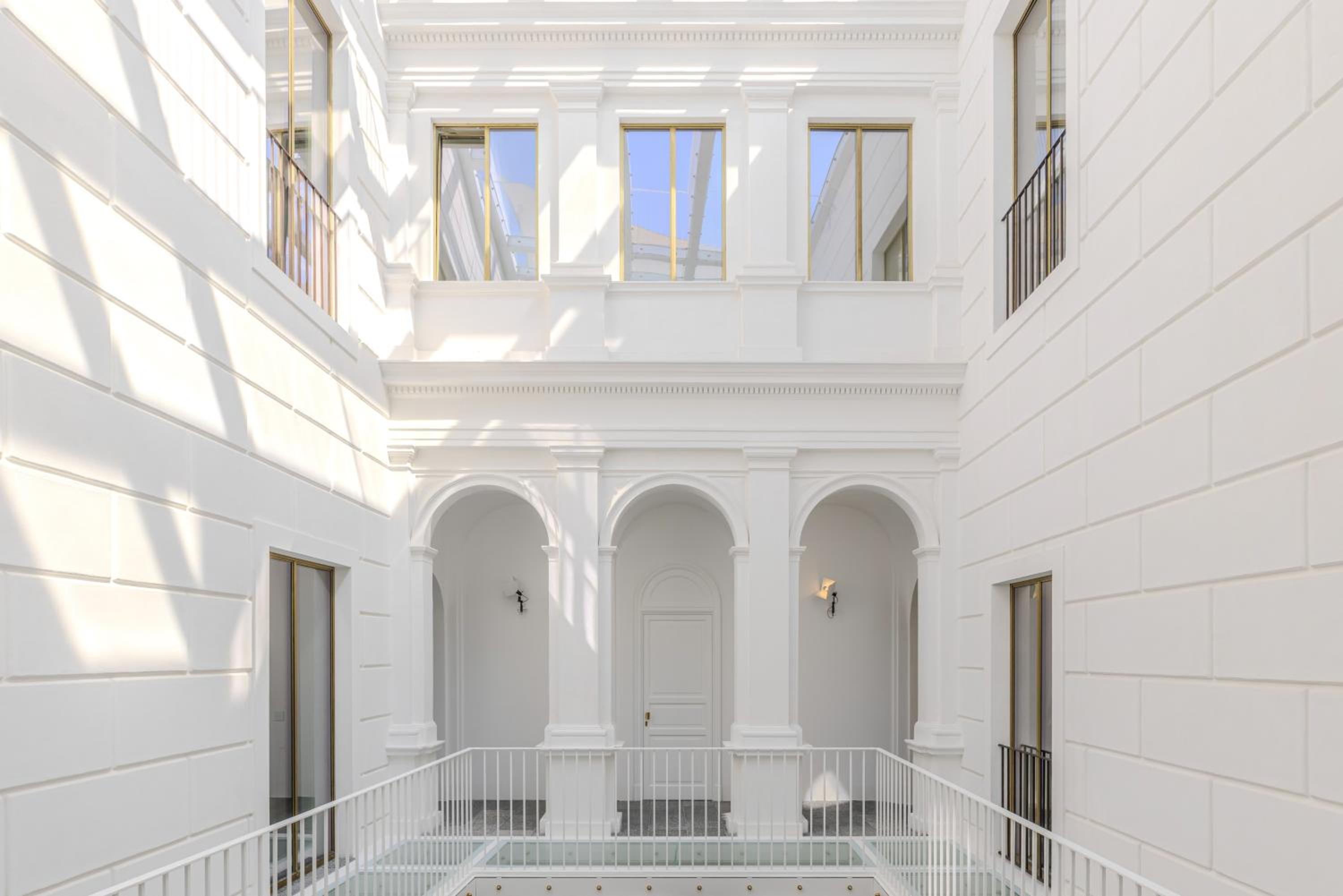 Sunlit white interior courtyard at Dome Hotel featuring neoclassical arches, columns, and upper-level windows.