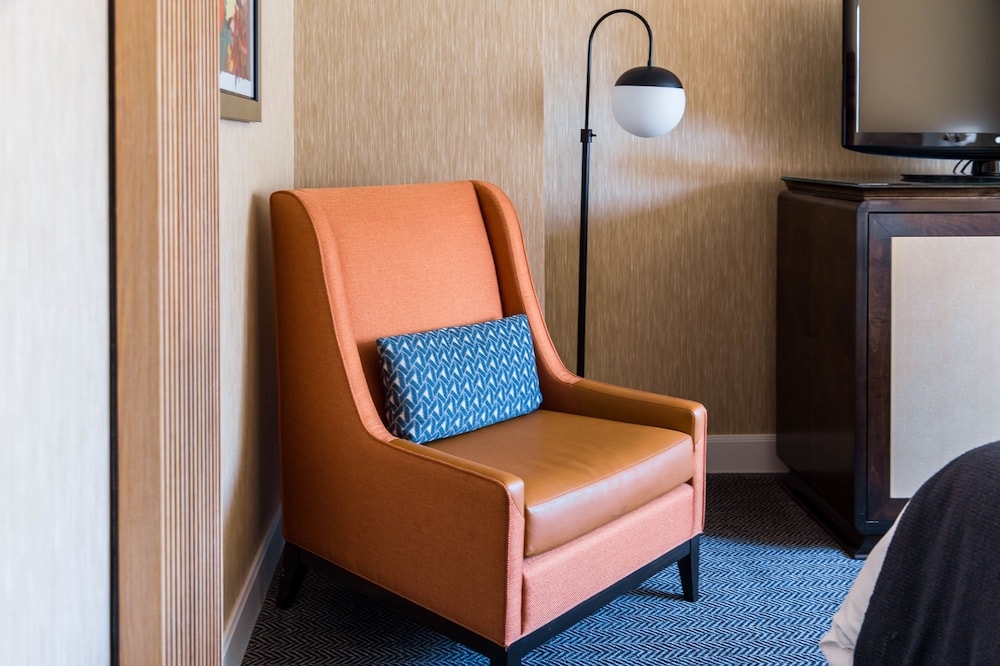 An orange armchair with a patterned blue pillow sits beside a modern floor lamp and a wooden console cabinet.