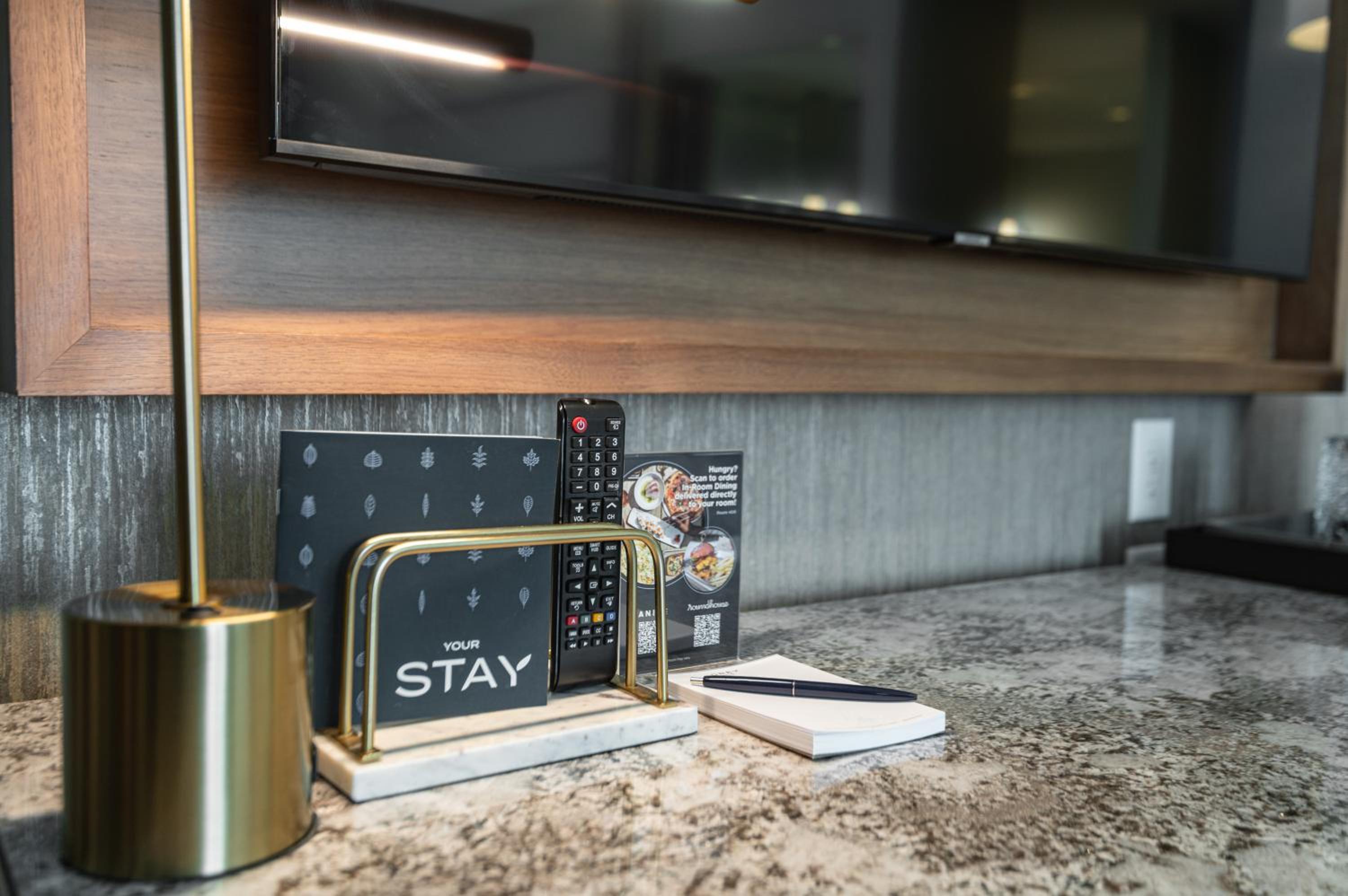 Granite countertop in a guest room featuring a brass lamp, a TV remote in a brass holder, and a notepad.