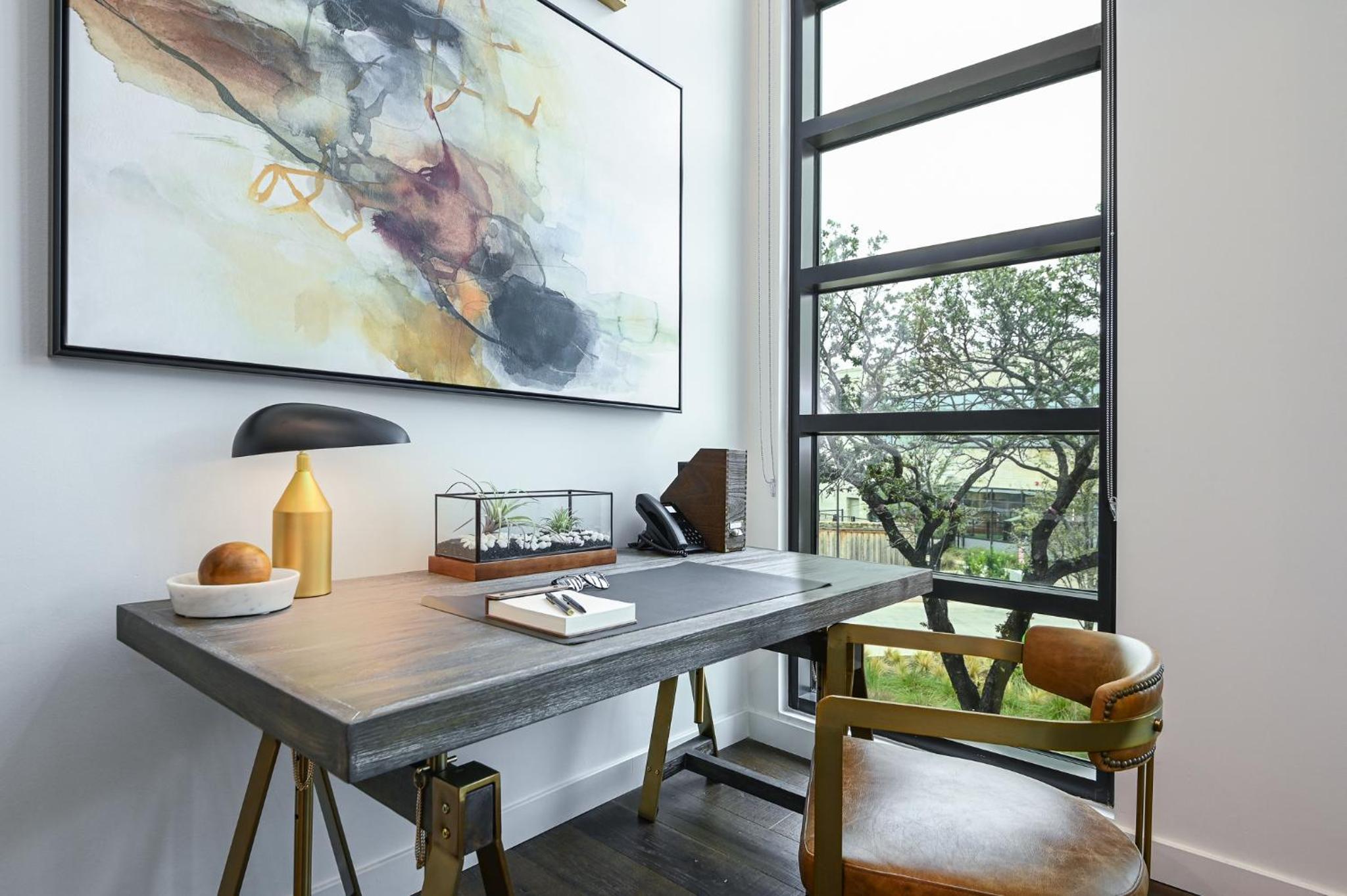 Wooden work desk paired with a leather chair beside a large window looking out onto tree branches.