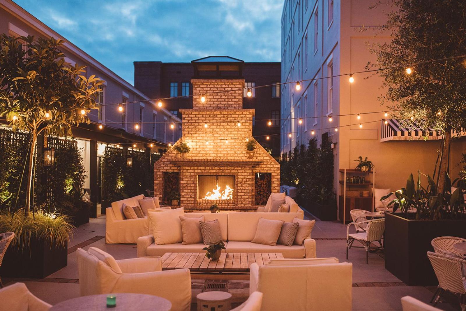 Outdoor courtyard terrace at Emeline at dusk, with string lights hung over white sofas and a roaring brick fireplace.