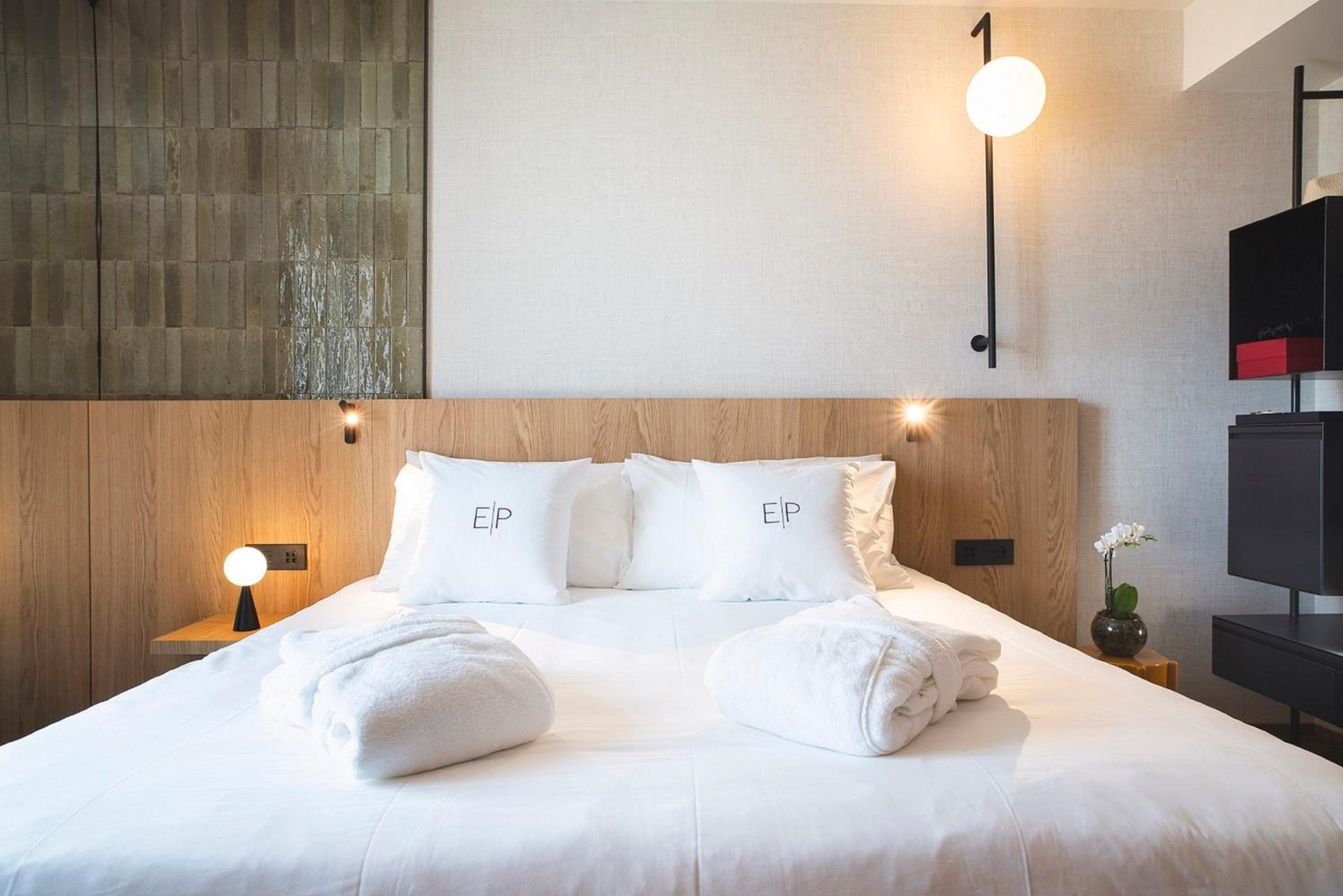 A bed dressed in white linens and monogrammed pillows against a light wood headboard with warm lighting.