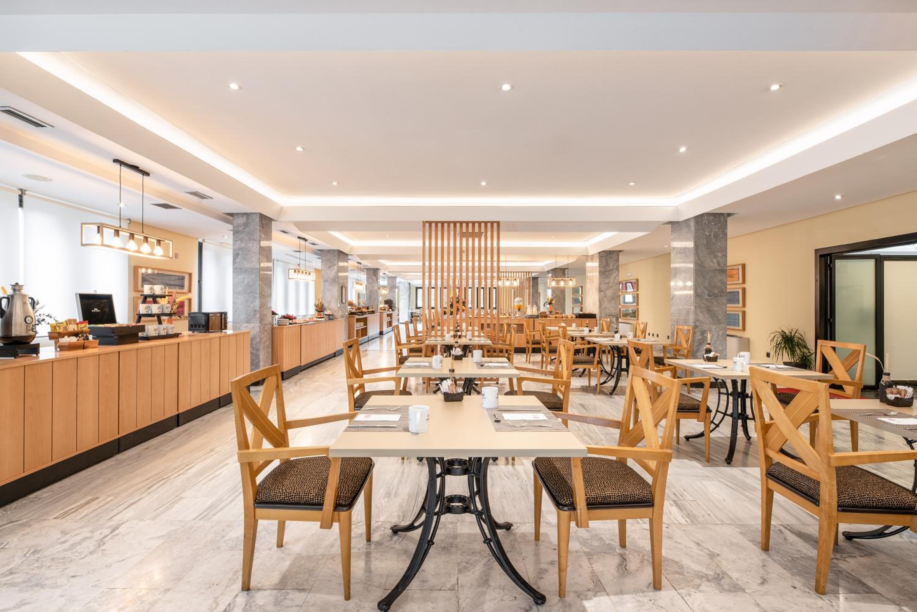 A dining room with marble flooring, wooden chairs at set tables, and buffet counters along the wall.