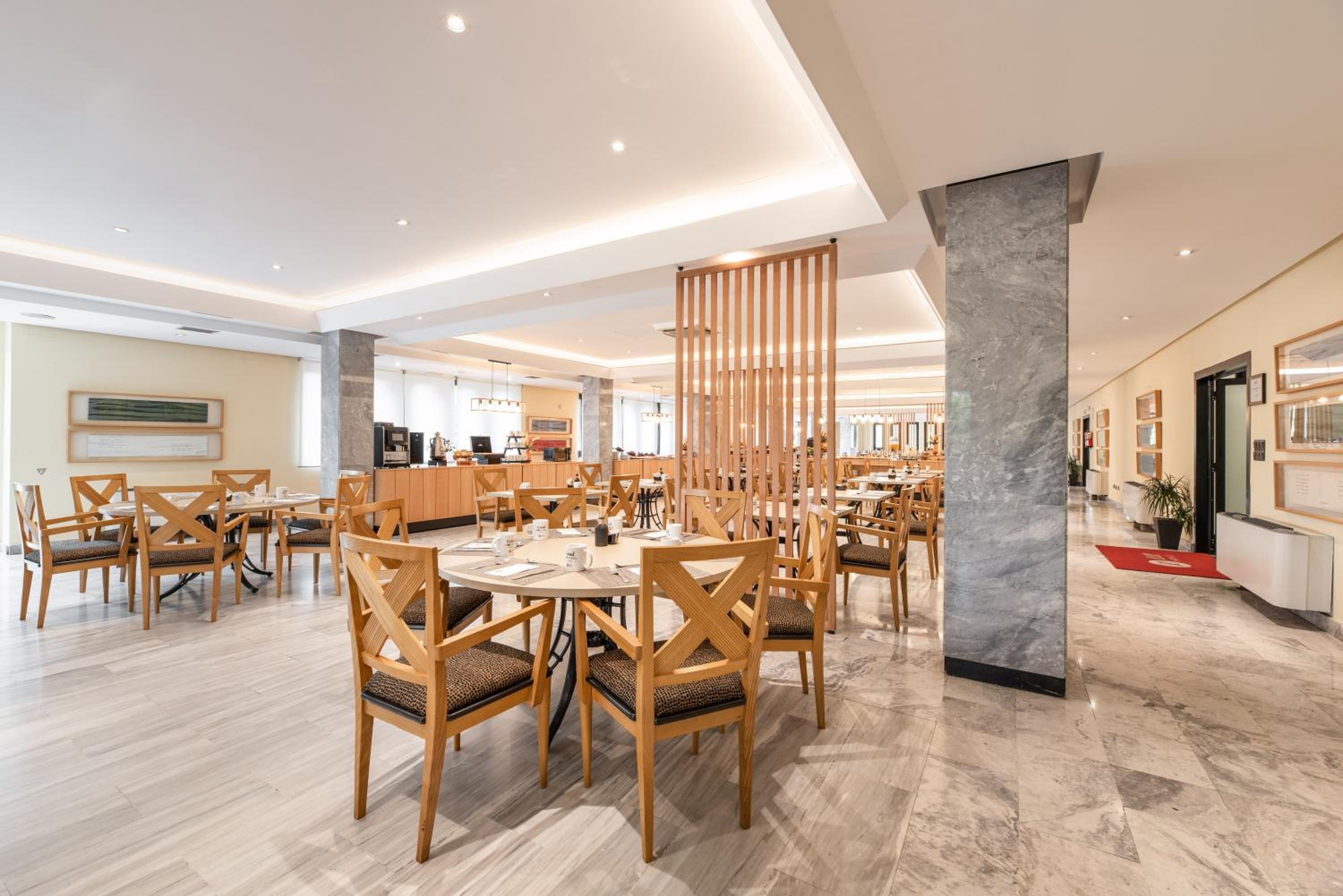 A dining area with round tables, cross-back wooden chairs, marble columns, and a slatted timber partition.