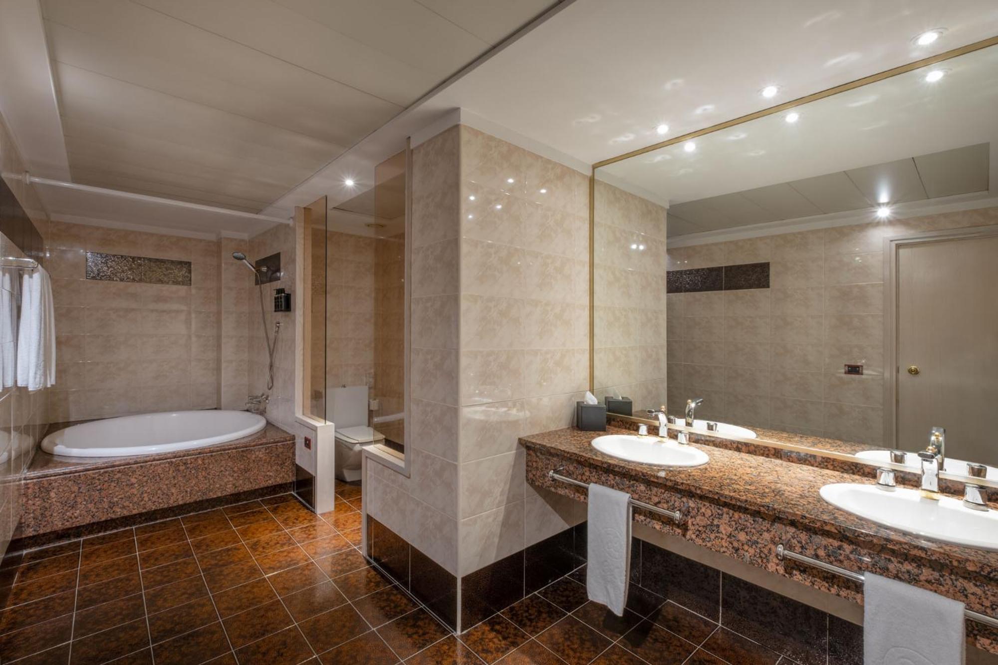 Bathroom with brown marble tiling, a sunken circular bathtub, and a vanity counter beneath a large mirror.