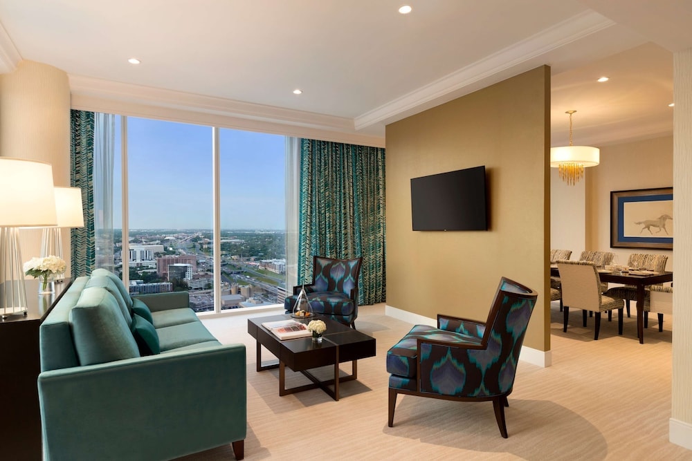 A Fairmont Austin suite living room with teal armchairs, sofa, wall-mounted TV, and wide window view.
