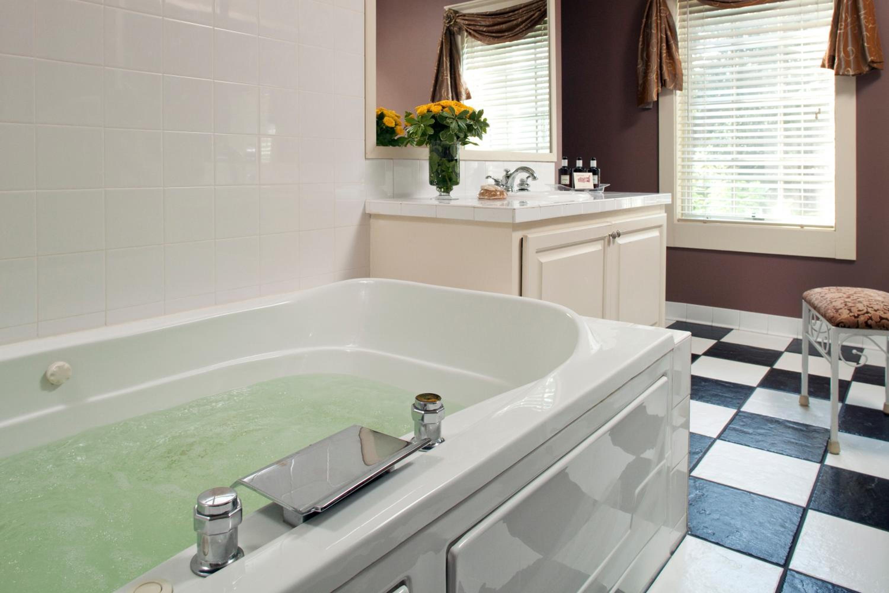 A bathroom with a filled jetted soaking tub, white vanity, and black-and-white checkered tile floor.
