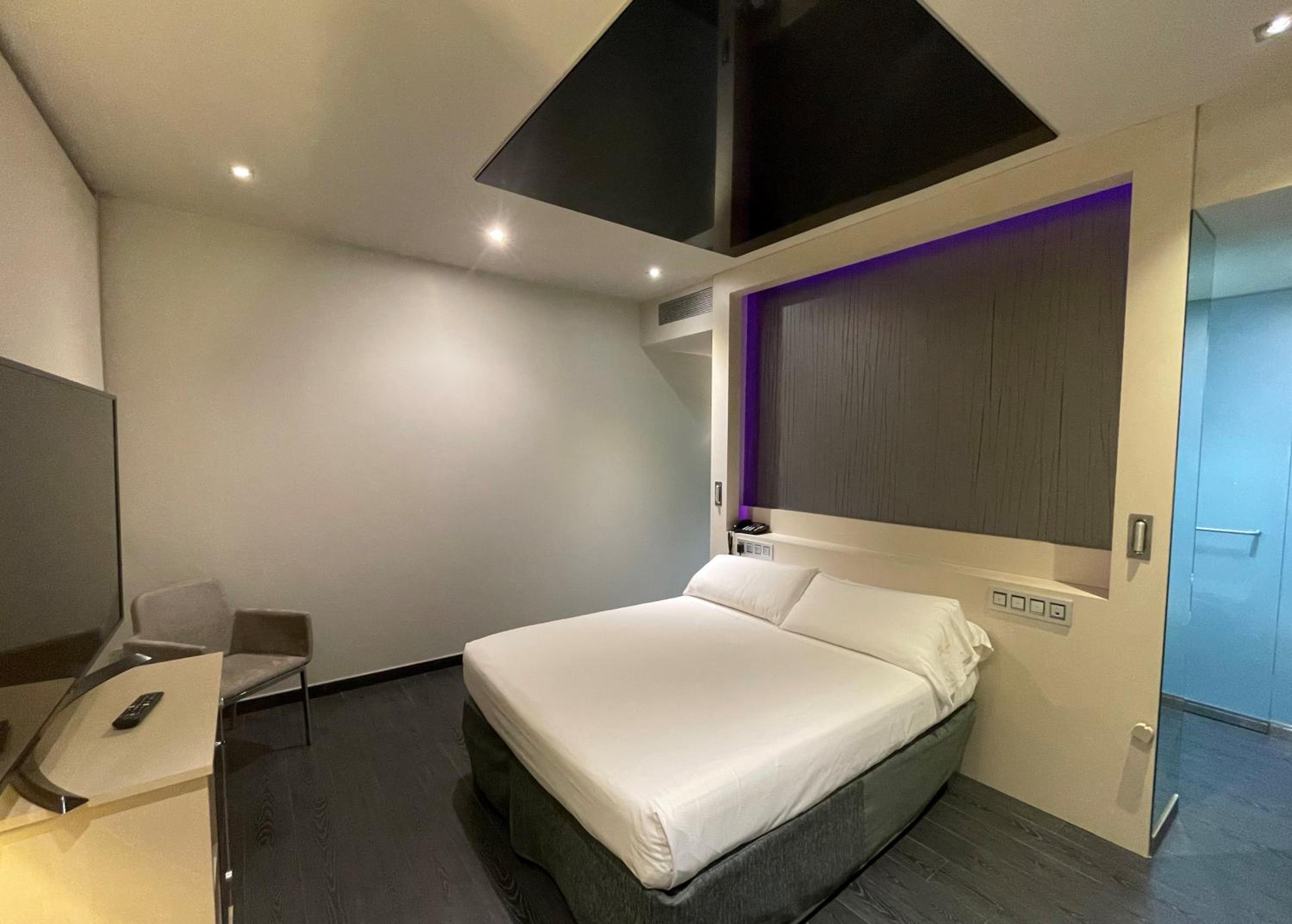 A bedroom with a made bed, dark wood flooring, and recessed purple lighting above the headboard.
