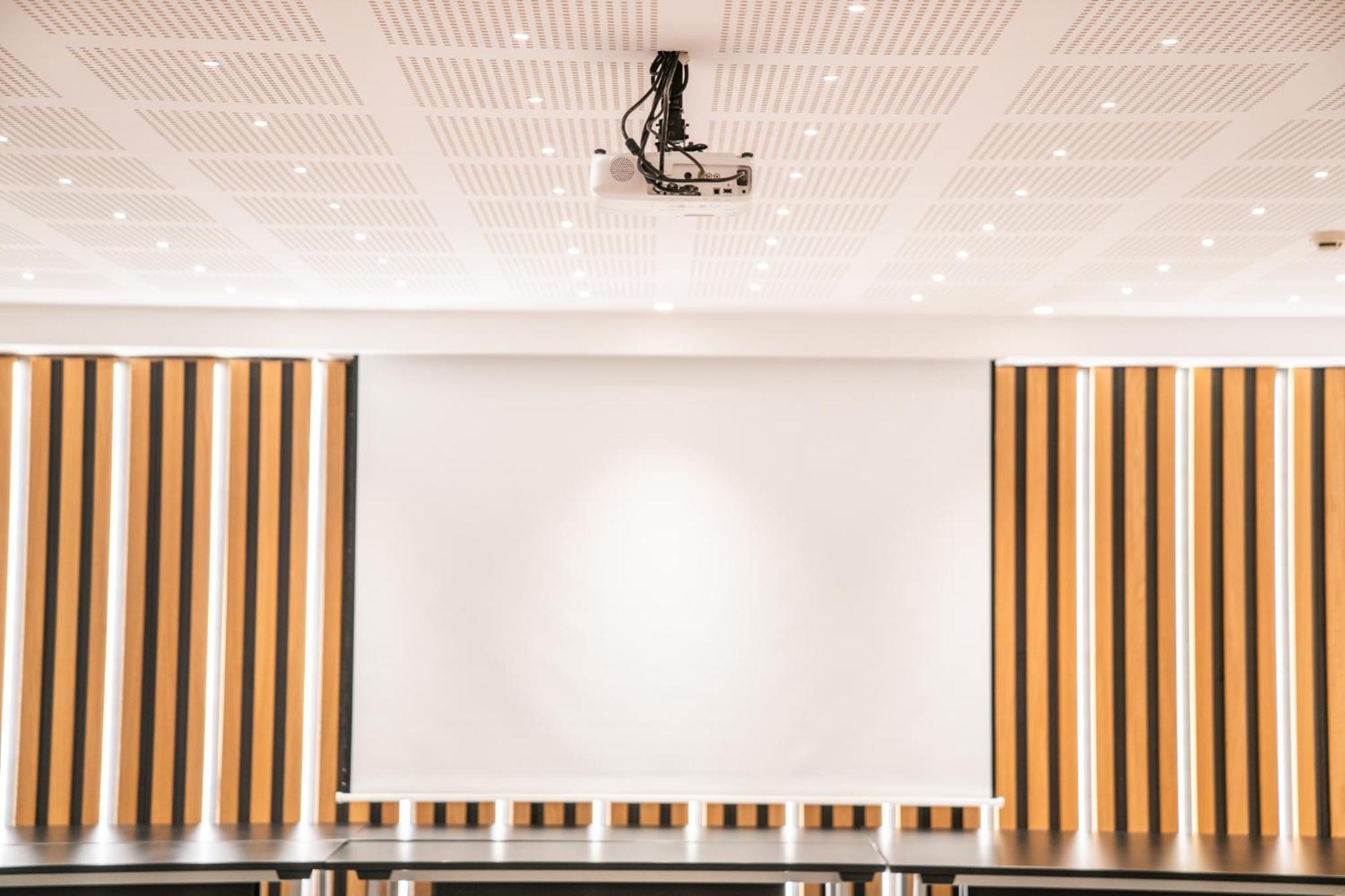 A ceiling-mounted projector faces a large white projection screen flanked by vertical wooden wall slats.