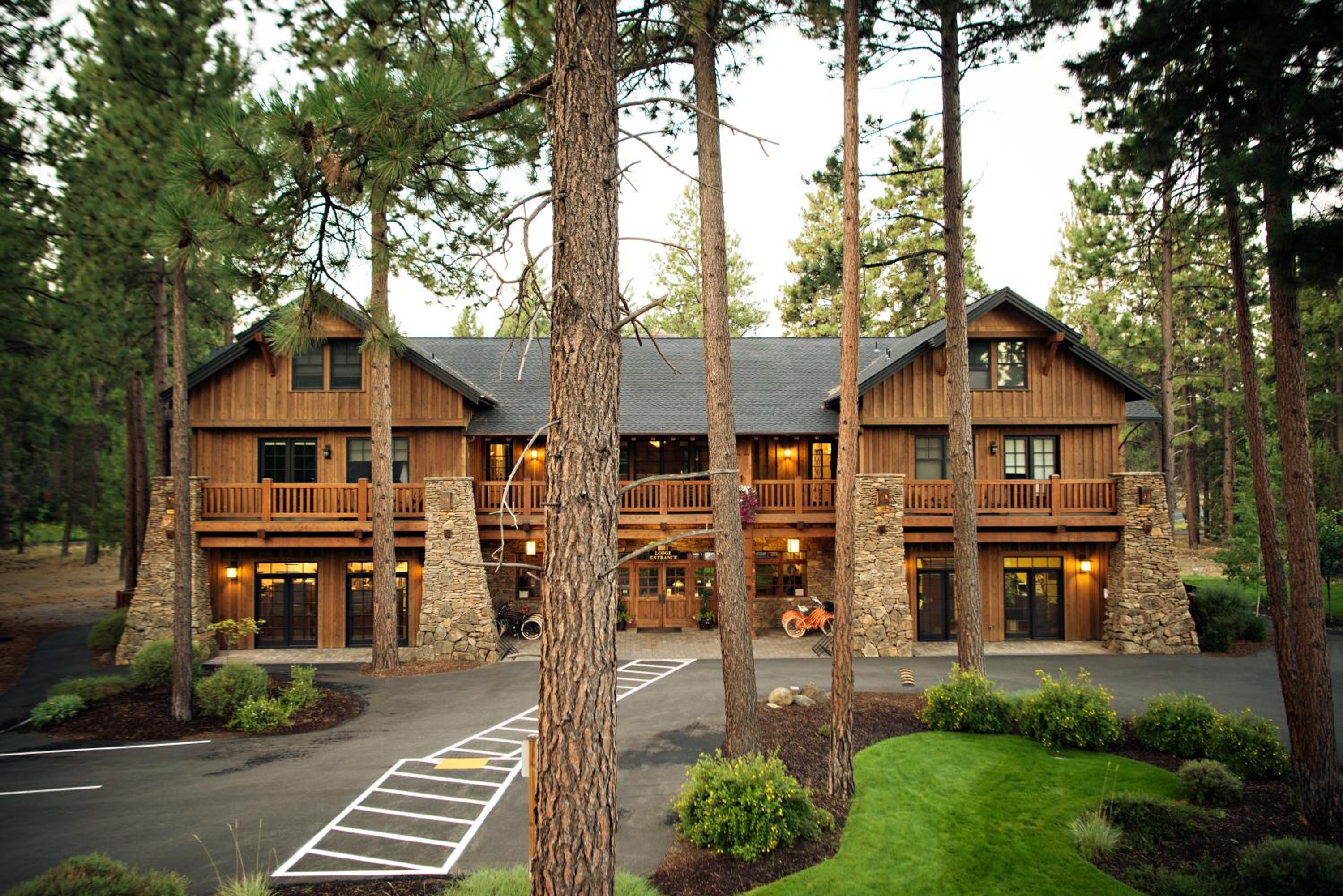 Exterior timber and stone facade of FivePine Lodge viewed through tall pine trees with a paved driveway.