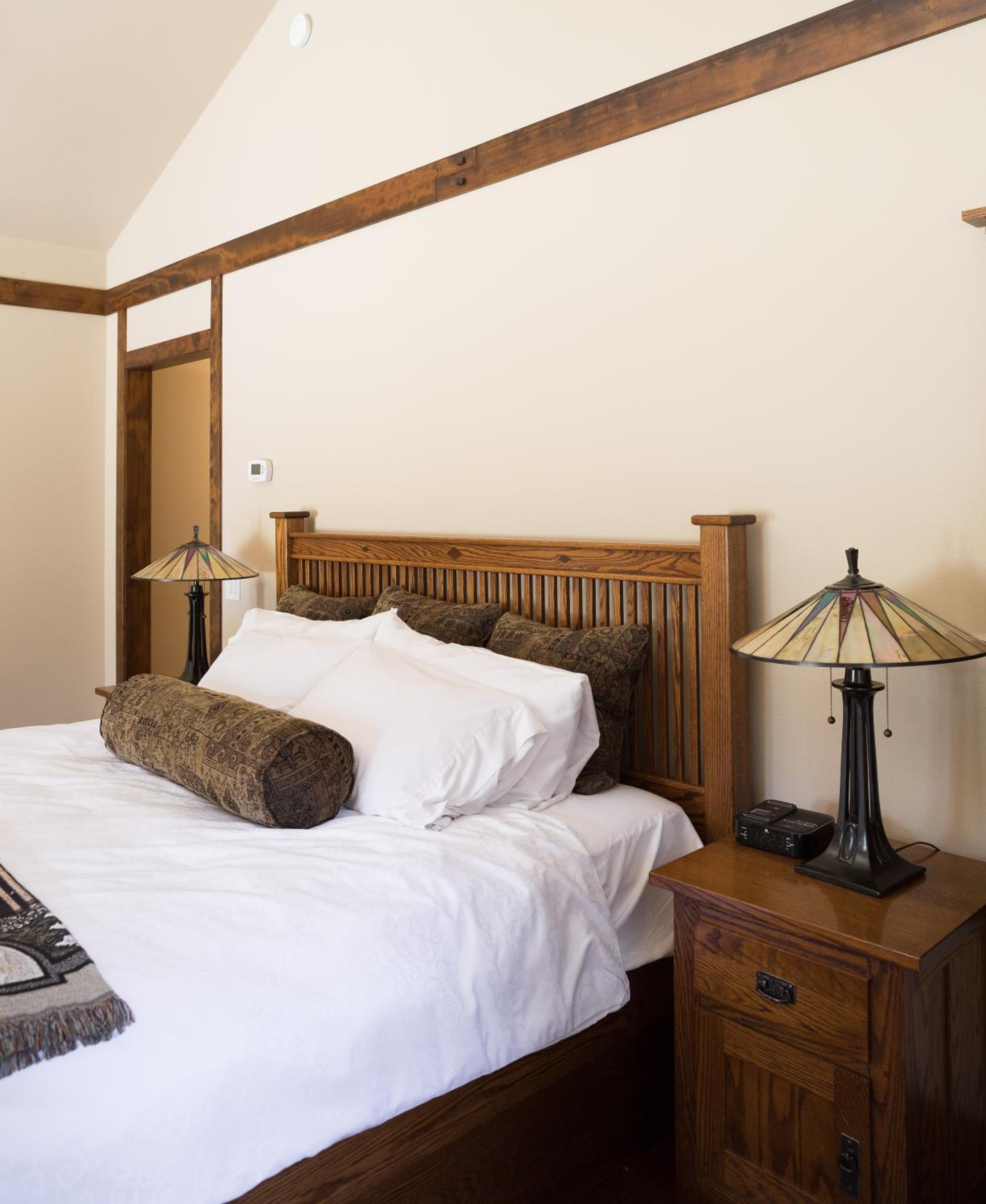 A bedroom with a slatted wooden headboard, white bedding, matching nightstands, and stained-glass lamps.