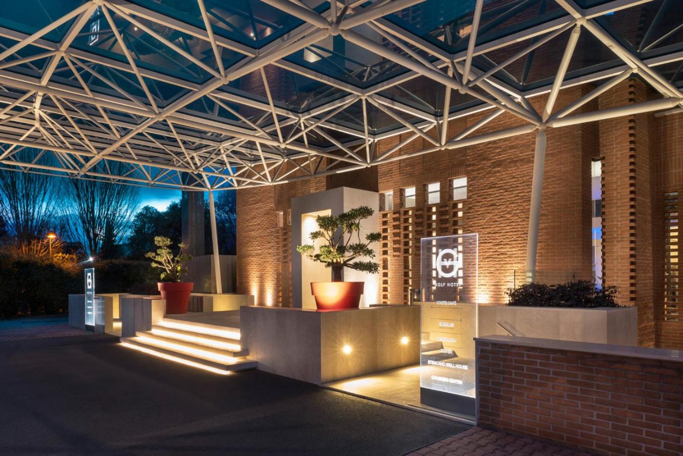 Illuminated night entrance of GHV Hotel beneath a geometric canopy, with brick facade and lit steps.