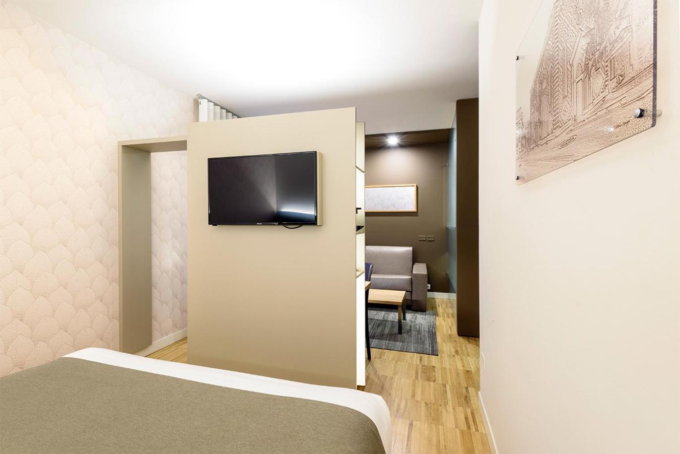 Hotel bedroom with a partition wall mounted with a television, revealing a sitting area with sofa beyond.