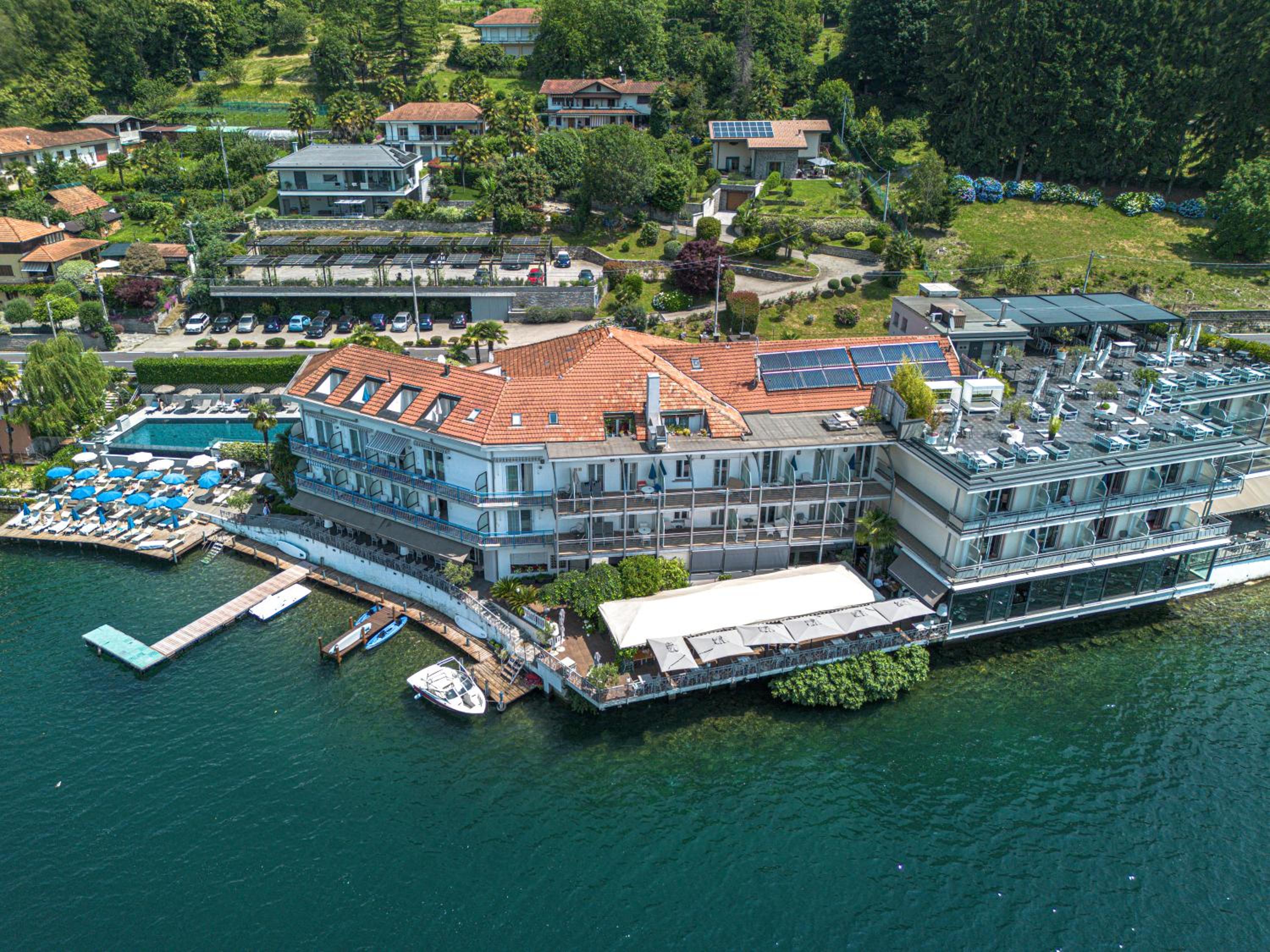Aerial view of the lakeside hotel complex surrounded by green hills, with a pool and wooden docks on the water.