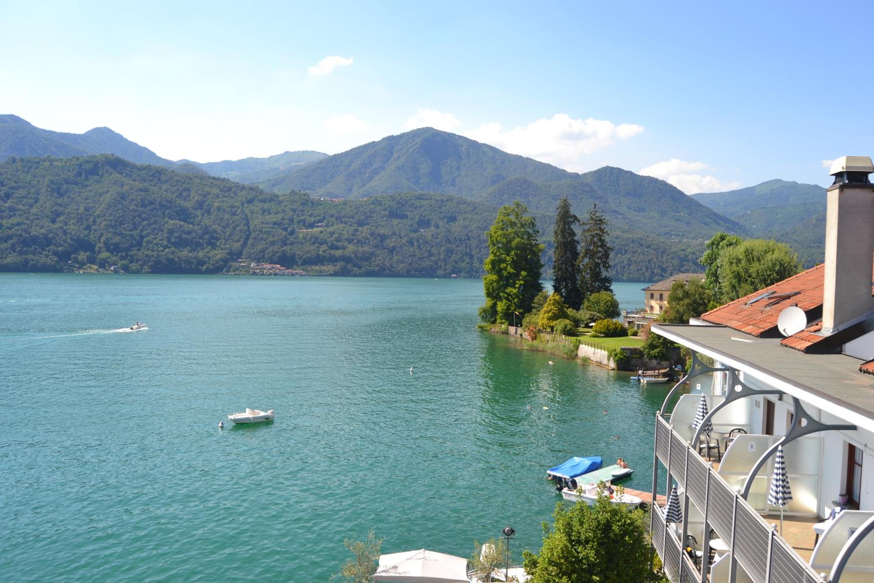 High-angle view from a balcony overlooking a wide lake and forested mountains under a blue sky.