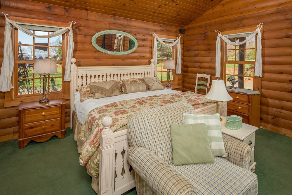 Log cabin bedroom with a painted wooden bed, green carpet, and a plaid armchair.