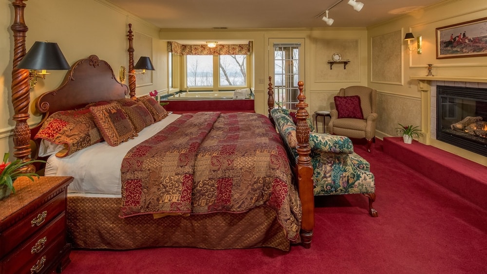 Bedroom with red carpet, a carved wooden bed, a fireplace, and a whirlpool tub by the window.