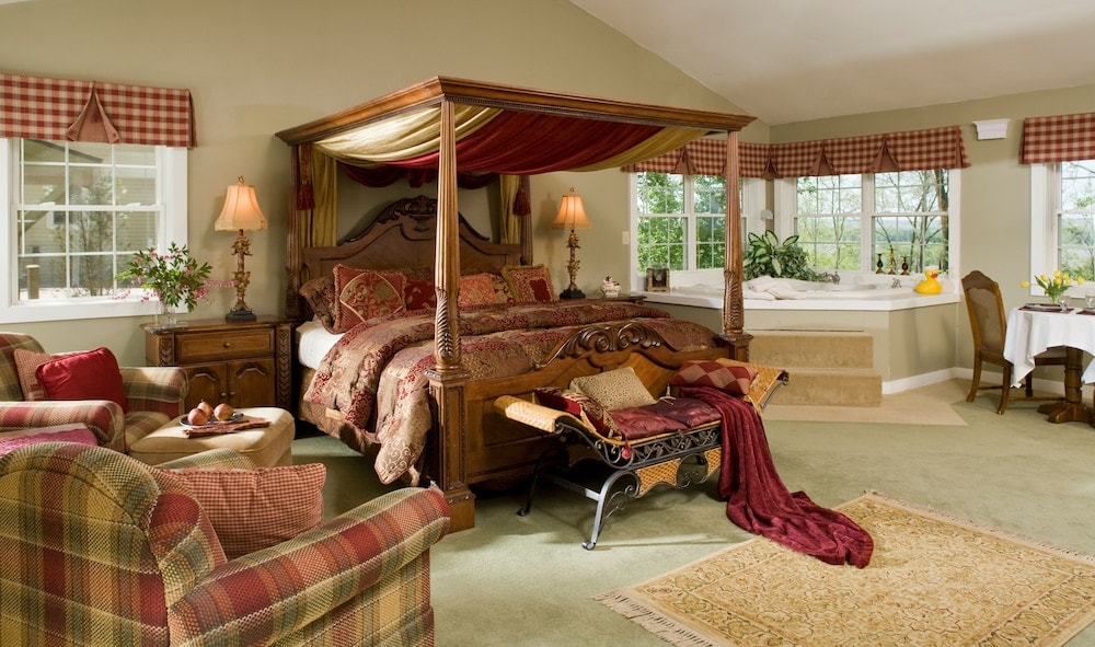 Suite with green carpet, a carved four-poster canopy bed, plaid armchairs, and a corner soaking tub.