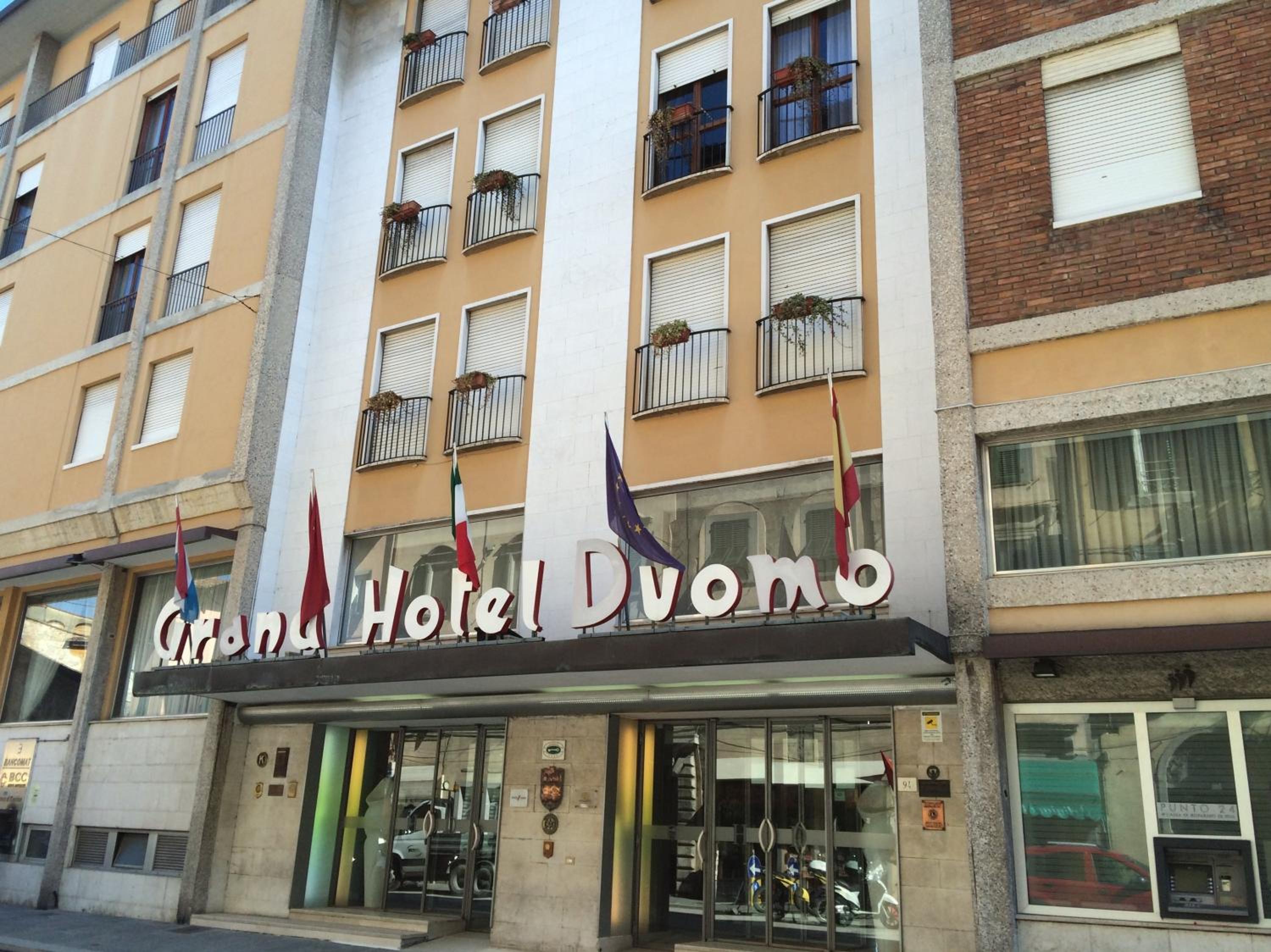 Facade and entrance of Grand Hotel Duomo with flags displayed beneath balconies.